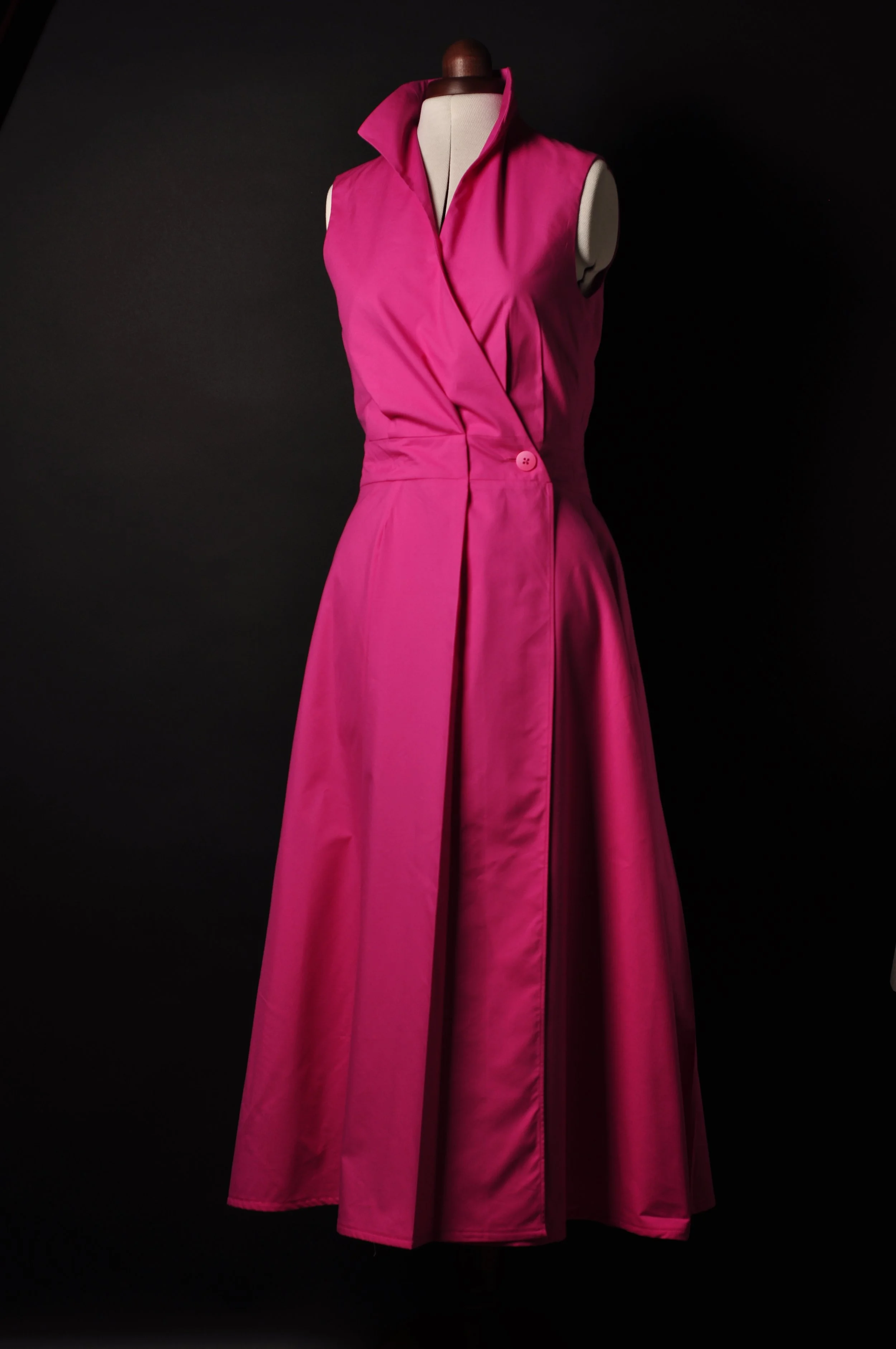 Langes ärmelloses Kleid in Fuchsia aus Baumwoll-Seiden-Mischung mit Kelchkragen, vorne mit Knopf zusammengehalten, schwarzer Hintergrund, präsentiert auf einer Schneiderpuppe.