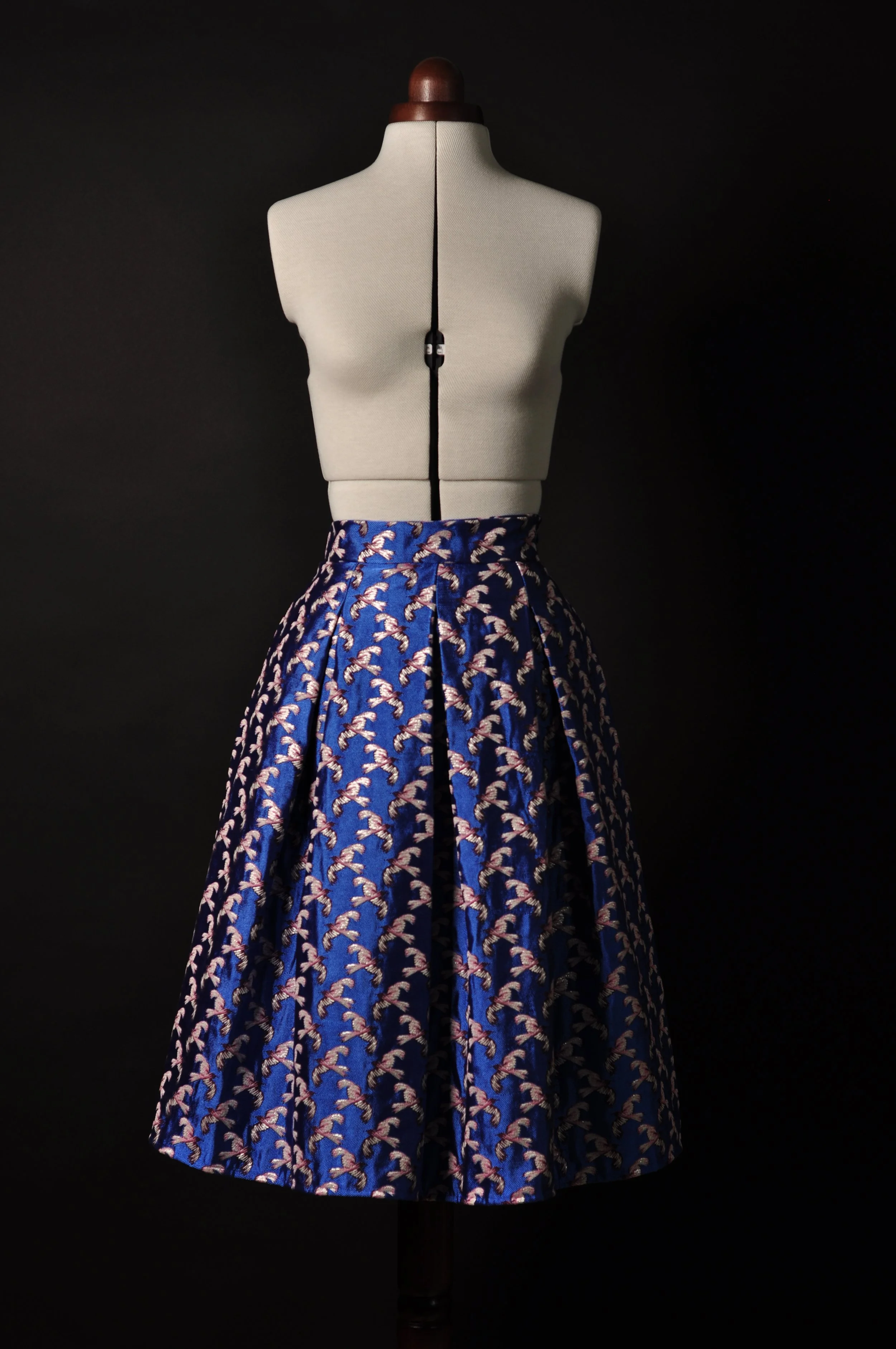 Schneiderpuppe mit blauem Rock mit weißen Vögeln gemustert vor schwarzem Hintergrund.