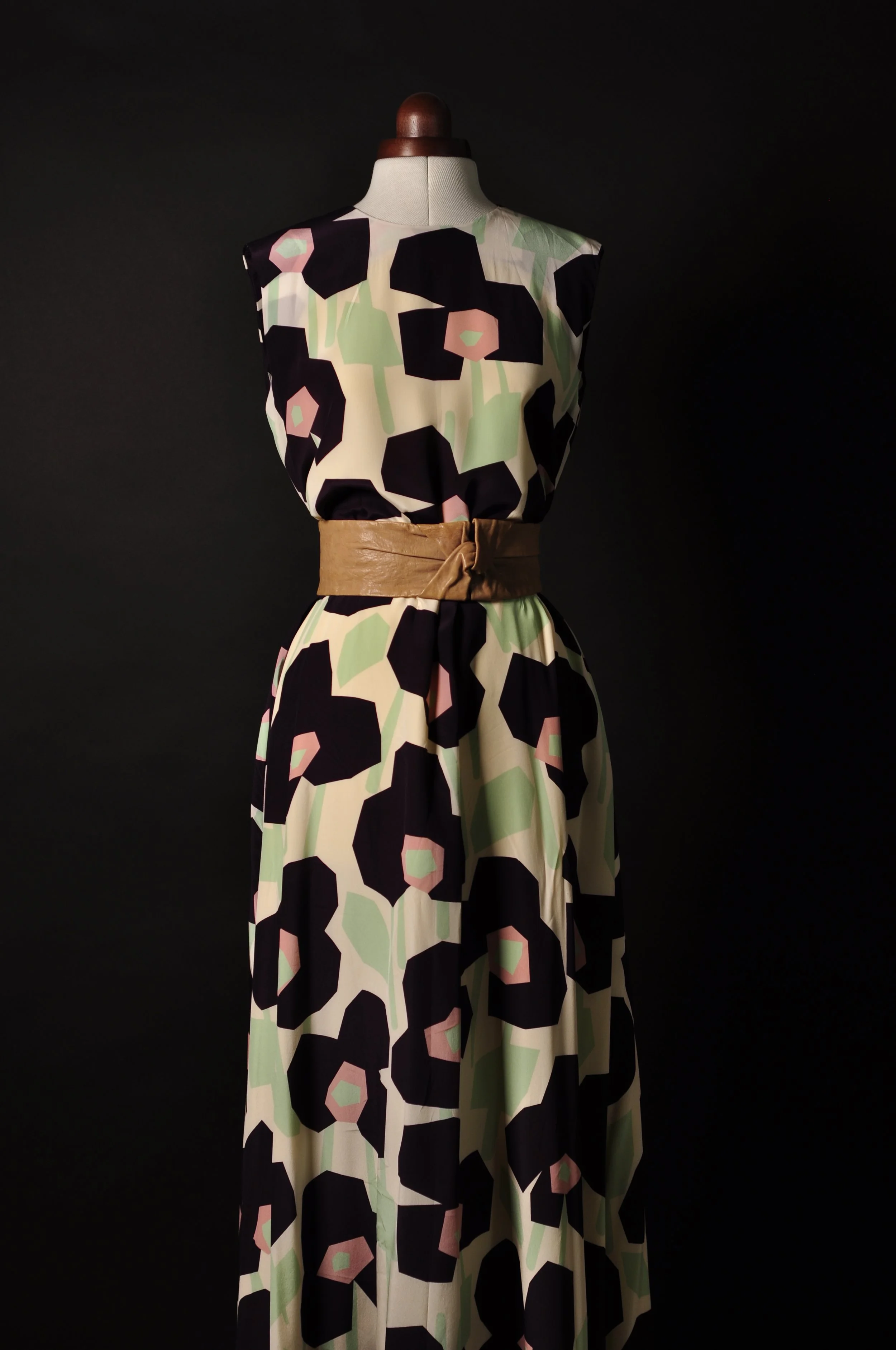 Schneiderpuppe mit langem, ärmellosem Kleid, floraler Print, brauner Gürtel, schwarzer Hintergrund.