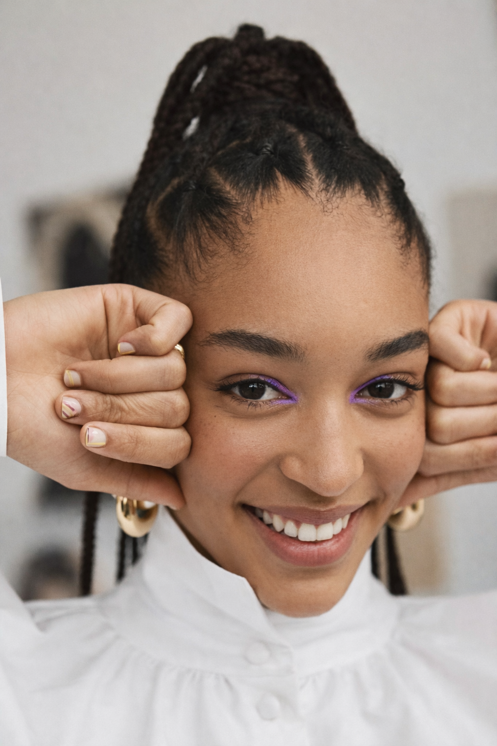 A woman with shoulder-length black hair smiling outdoors, wearing a blue top, with green plants in the background.