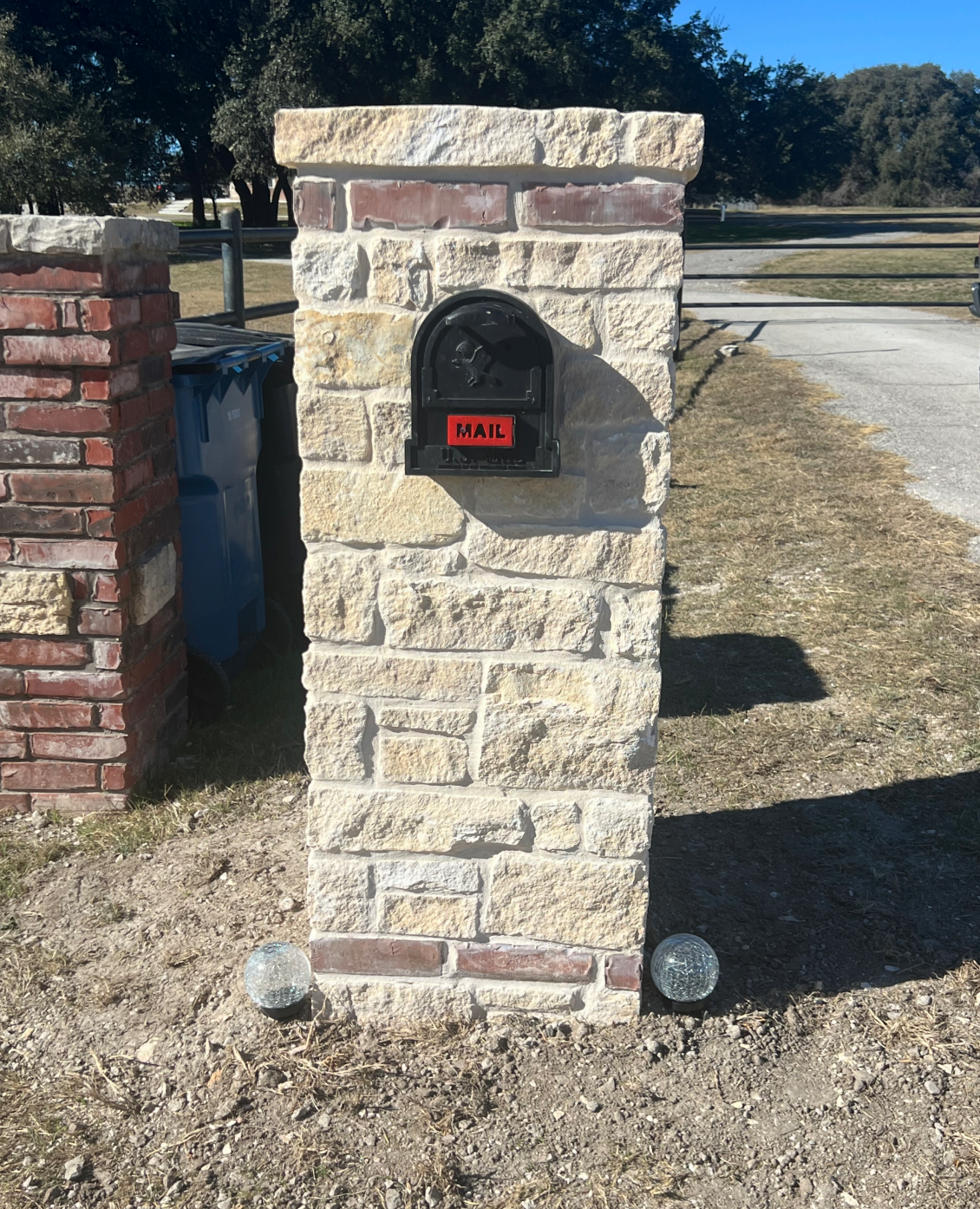 A black mailbox mounted on a stone and brick post with a red