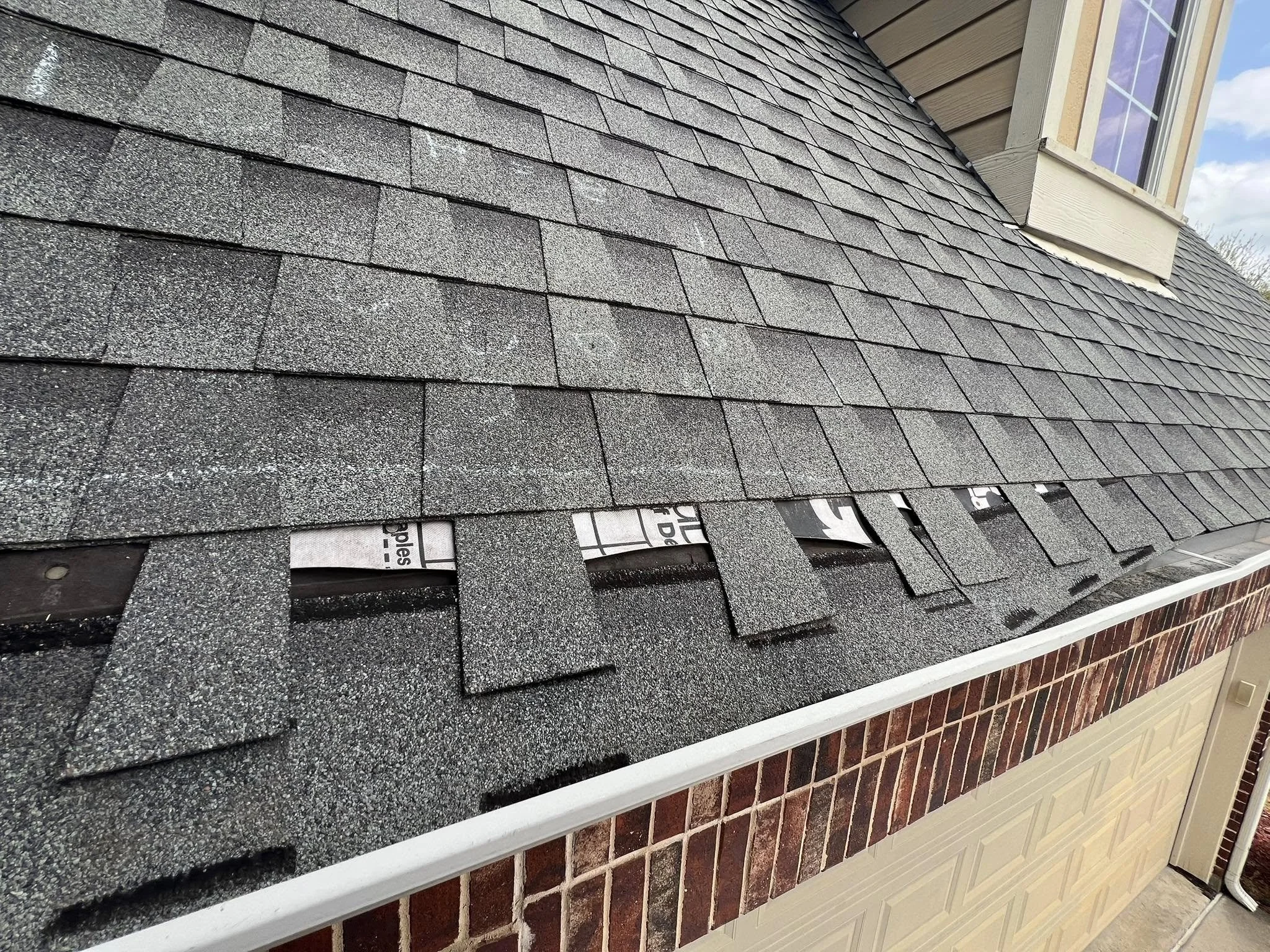 Close-up of a roof in the process of being shingled, with some shingles already installed and a few gaps revealing the underlayment.