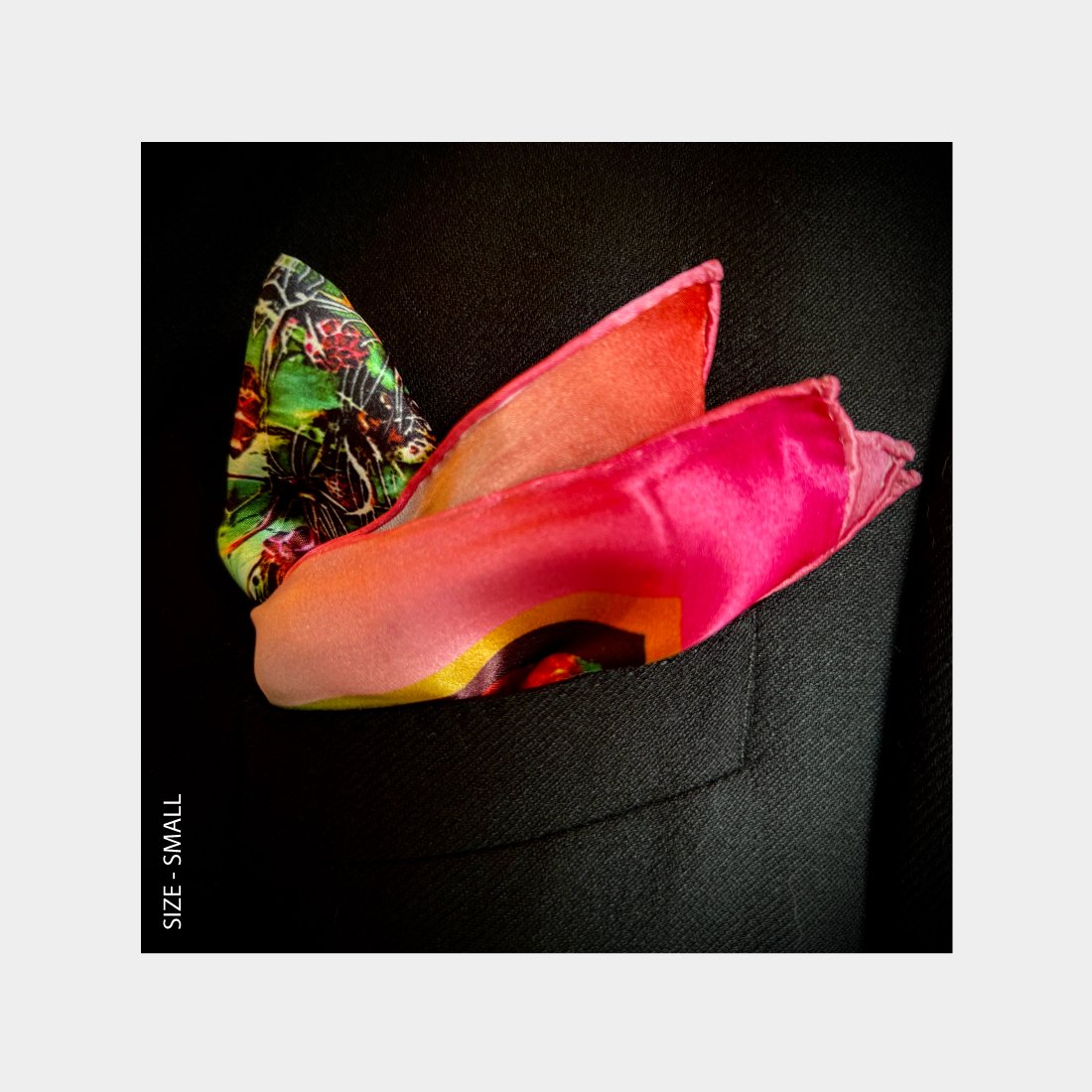 "Phoenix" is shown as a Pocket Square bursting with vibrant pinks and reds from the breast pocket of a black wool jacket.