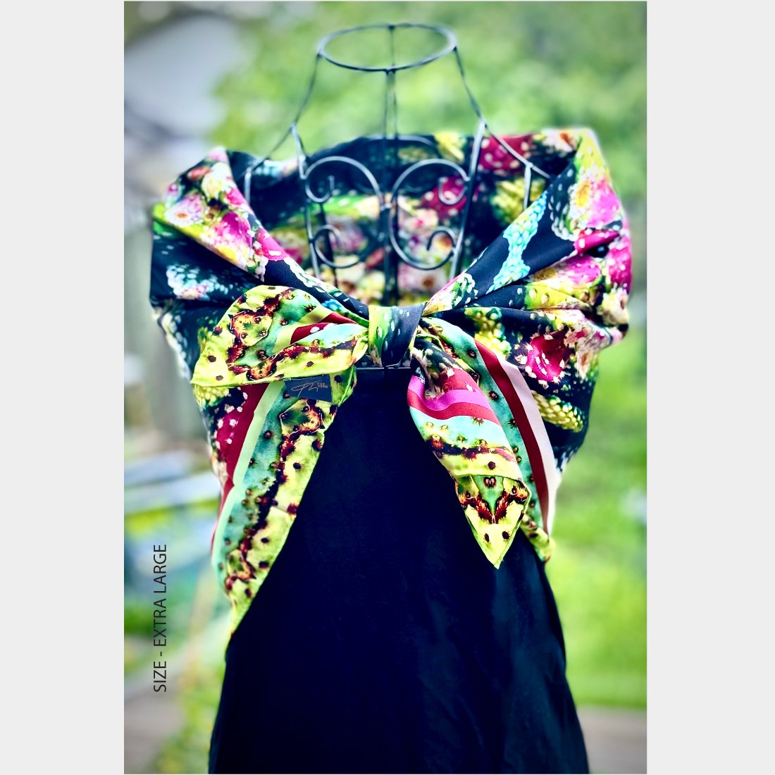 Mannequin wearing "Exotic Fruit" silk scarf, size extra large, tied like a bow at the bodice of a black sleeveless dress