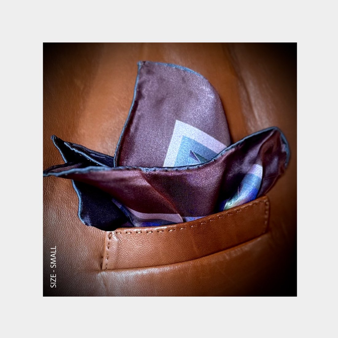 "Centuries of Healing" is shown as a silk Pocket Square flowering with rich purples from the breast pocket of a rich brown leather jacket.