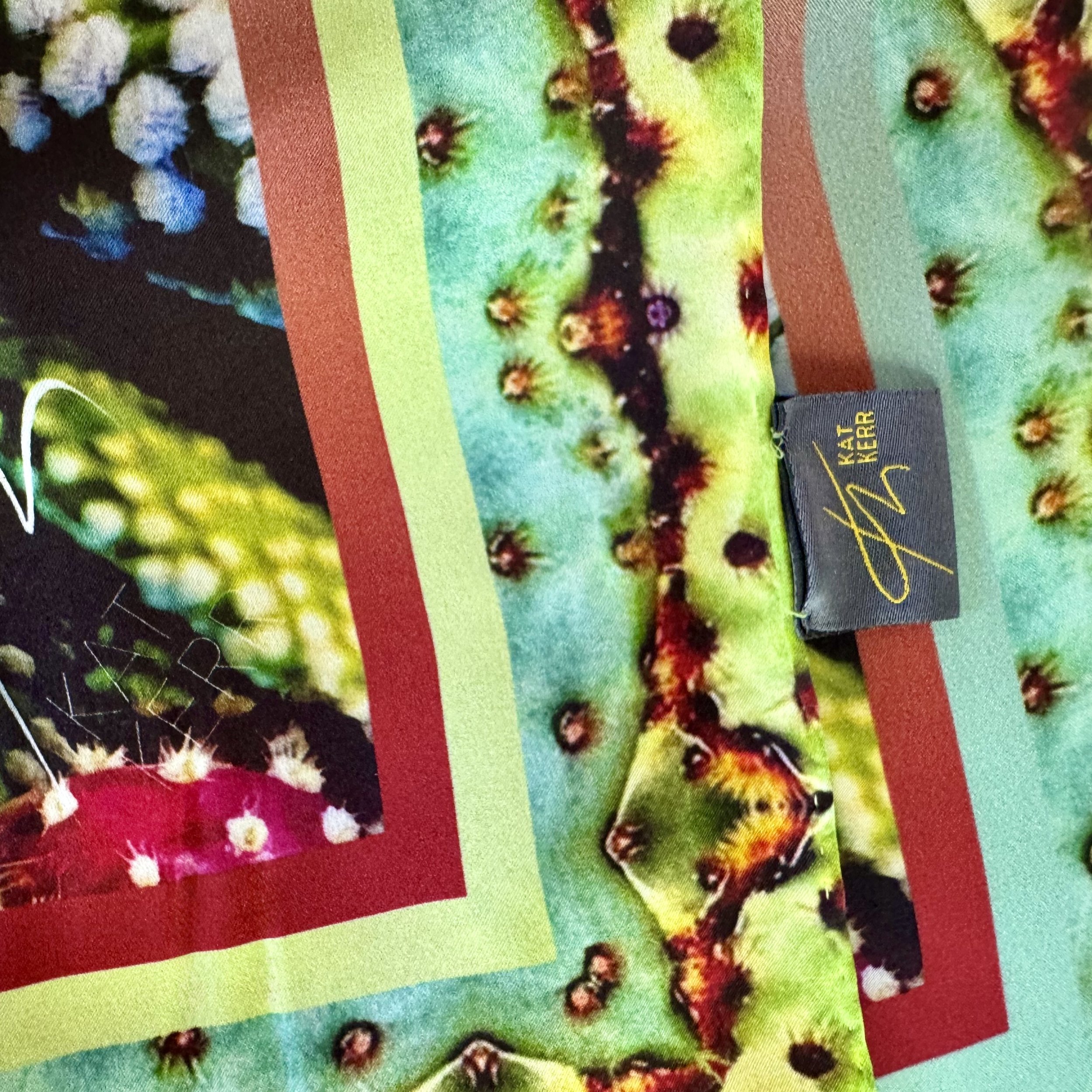 Corner edge of "Exotic Fruit" silk scarf showing intricate edge design, double sided printing, texutre, logo and label