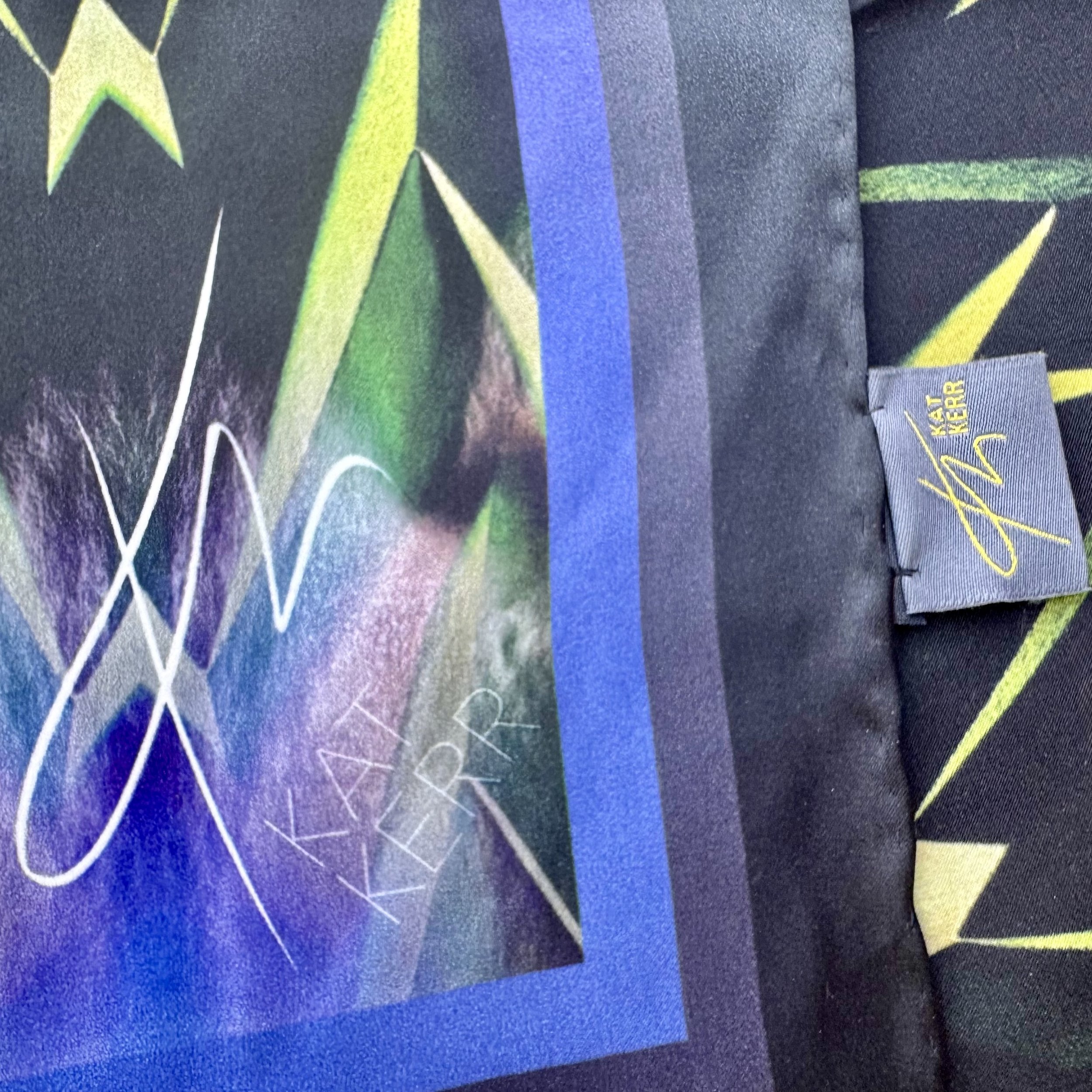 Detail of "Centuries of Healing" silk scarf showing double sided printing, satin texture, colour, hand sewn edges, logo and label