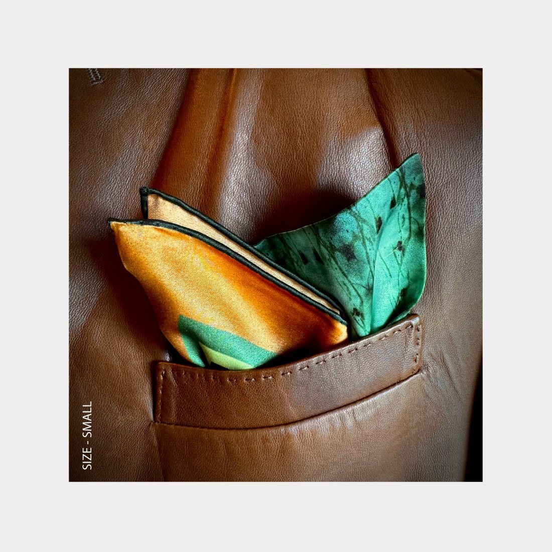 "Quenched" is shown is a Pocket Square folded as a pop of teal and orange pattern in the breast pocket of a copper leather jacket.