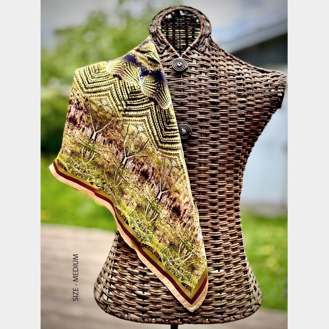 "Roots" silk scarf in size medium is shown draped in a triangular shape over one shoulder of a wicker mannequin.