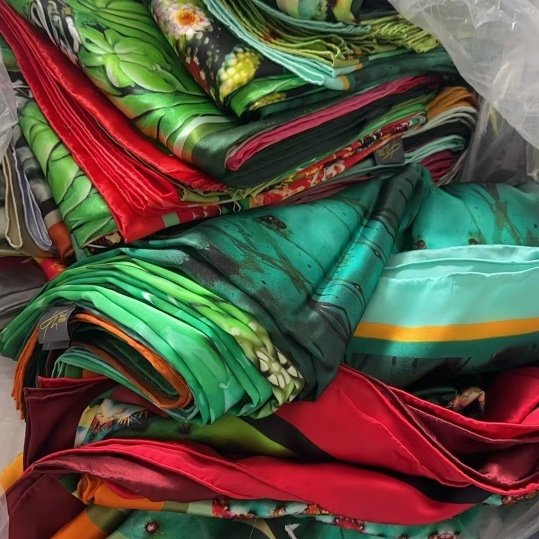 Stack of colorful silk scarves in jewel tones with floral and abstract patterns.