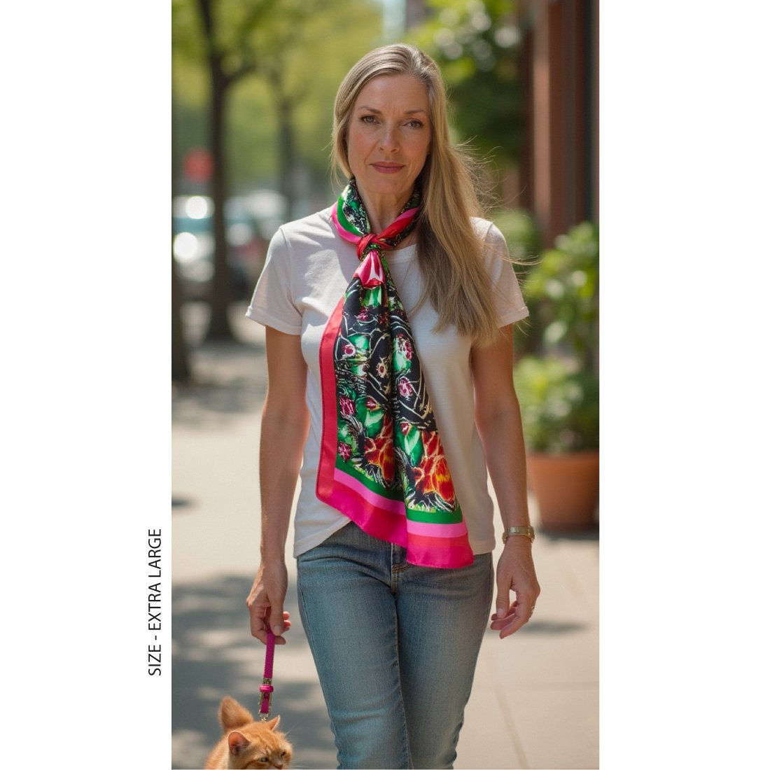 A woman with long blond hair is walking her cat win a park. She is wearing a white t-shirt and jeans, styled with a beautiful large silk scarf tied around her neck and dangling down to her waist.