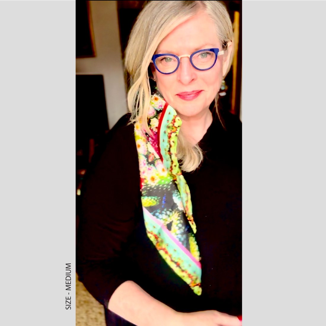 A woman ina black outfil smiles at the camera. Exotic Fruit silk scarf in size medium is tied in her hair and draped over her shoulder.