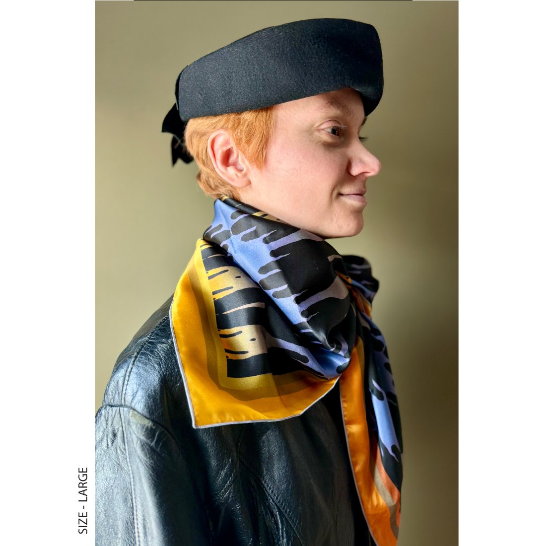 A woman with short red hair is wearing a contemporary scarf in oranges and blues