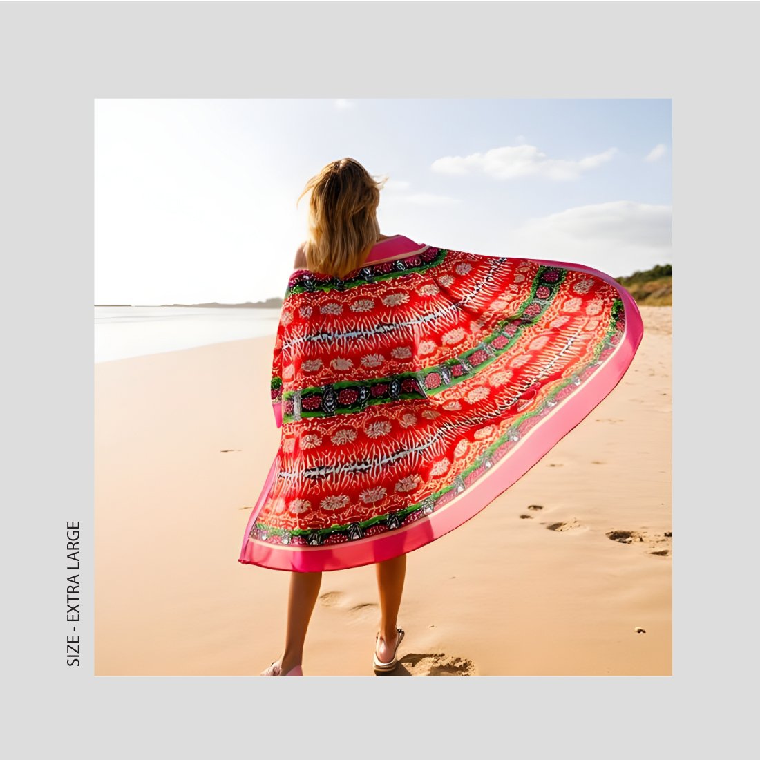 A woman hold out the extra large vibrant red pattern scarf she is wearing at the beach.