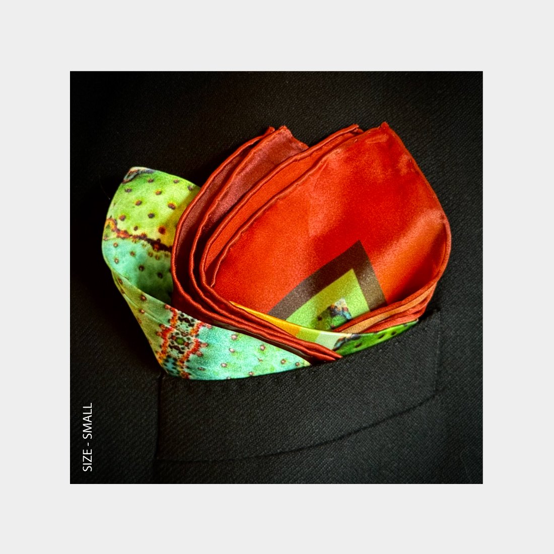 "Like Beadwork" is shown is a Pocket Square folded as a pop of green and red pattern in the breast pocket of a black wool jacket.