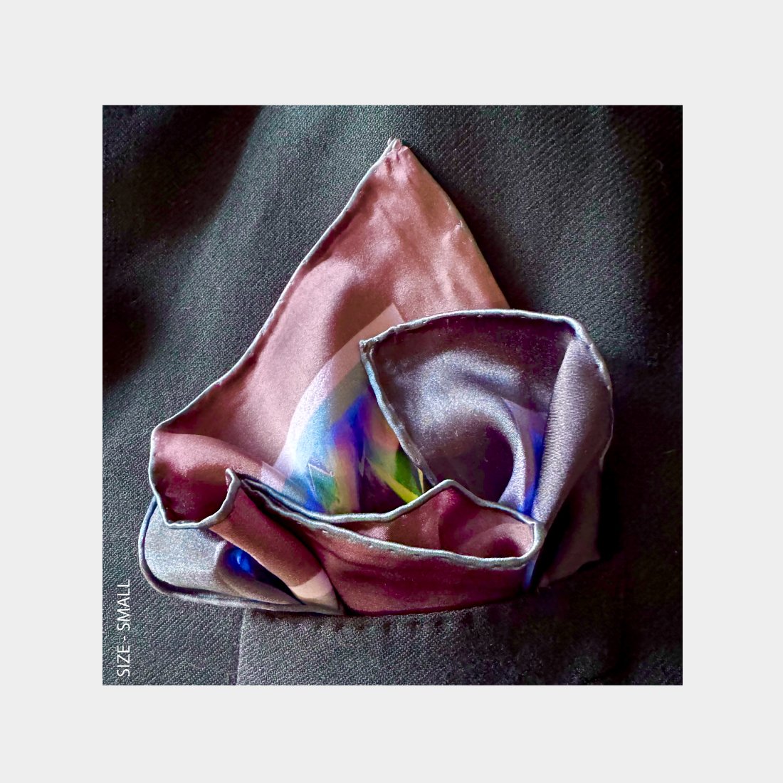 "Centuries of Healing" is shown as a silk Pocket Square flowering with rich purples from the breast pocket of a black wool jacket.