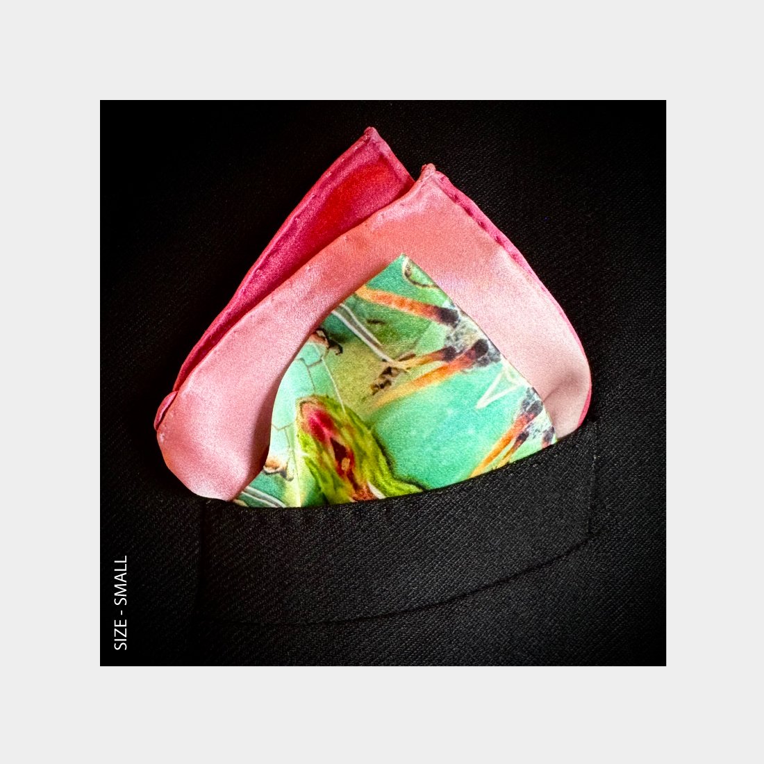 "Arizona"" is shown as a Pocket Square offering a burst of pink, mauve, and teal, from the breast pocket of a black wool suit jacket.
