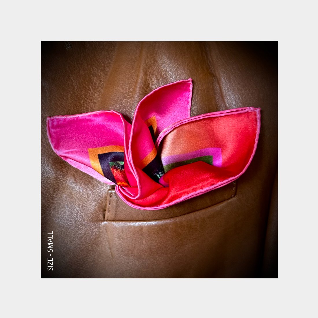 "Phoenix" is shown as a Pocket Square bursting with vibrant pinks and reds from the breast pocket of a copper leather jacket.
