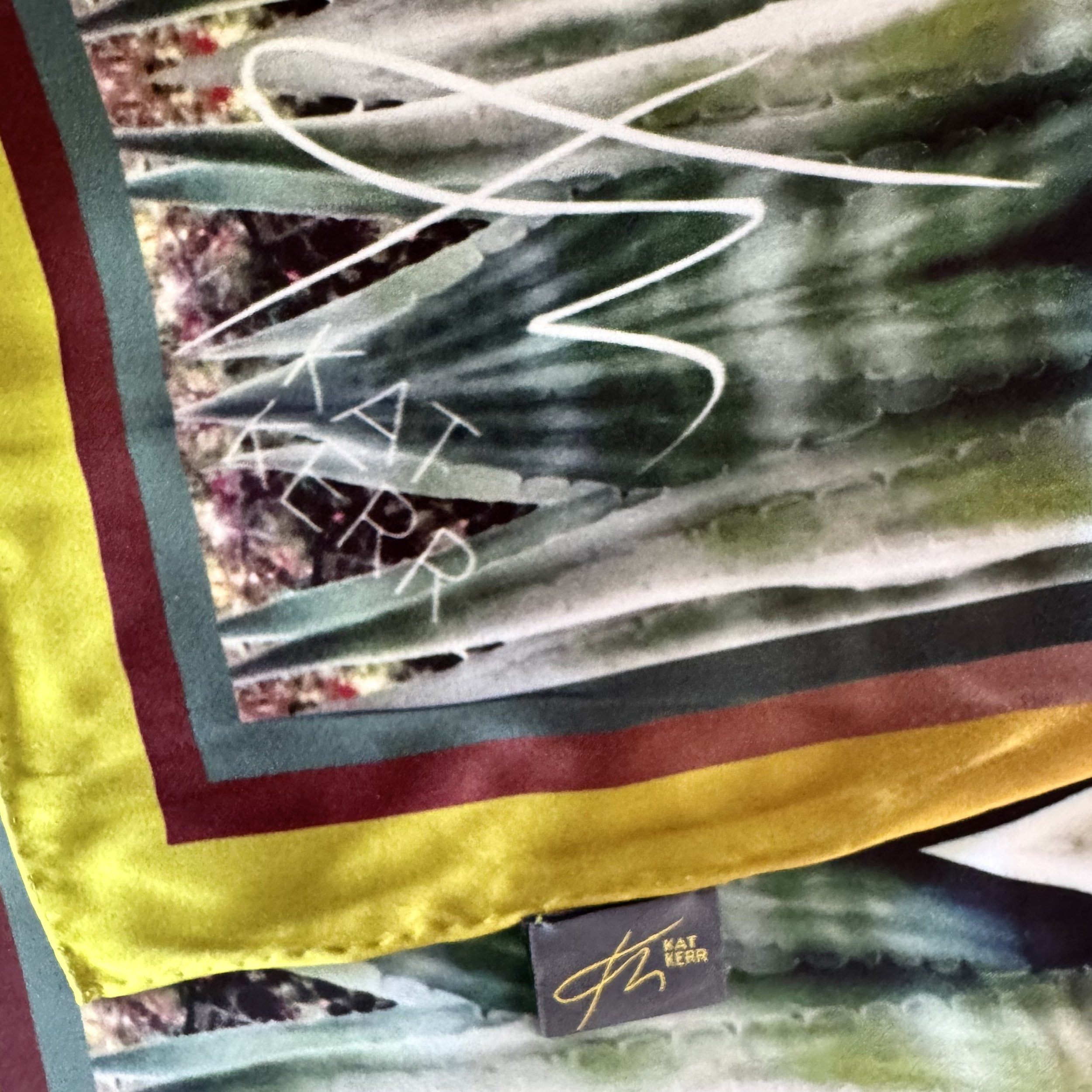 Corner edge of "Metamorphosis" silk scarf showing textures, double sided printing, hand sewn edging, label and logo