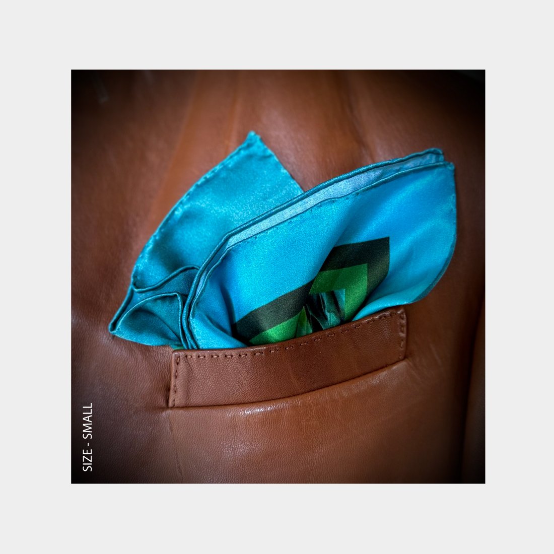 "The Life of Water" is shown as a silk Pocket Square flowering with jewelled toned blues and greens from the breast pocket of a brown leather jacket.