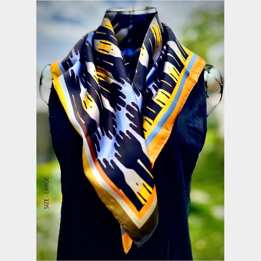 "Sunset Sentinels" slik scarf size large is draped over the shoulders of a wire mannequin in a black top