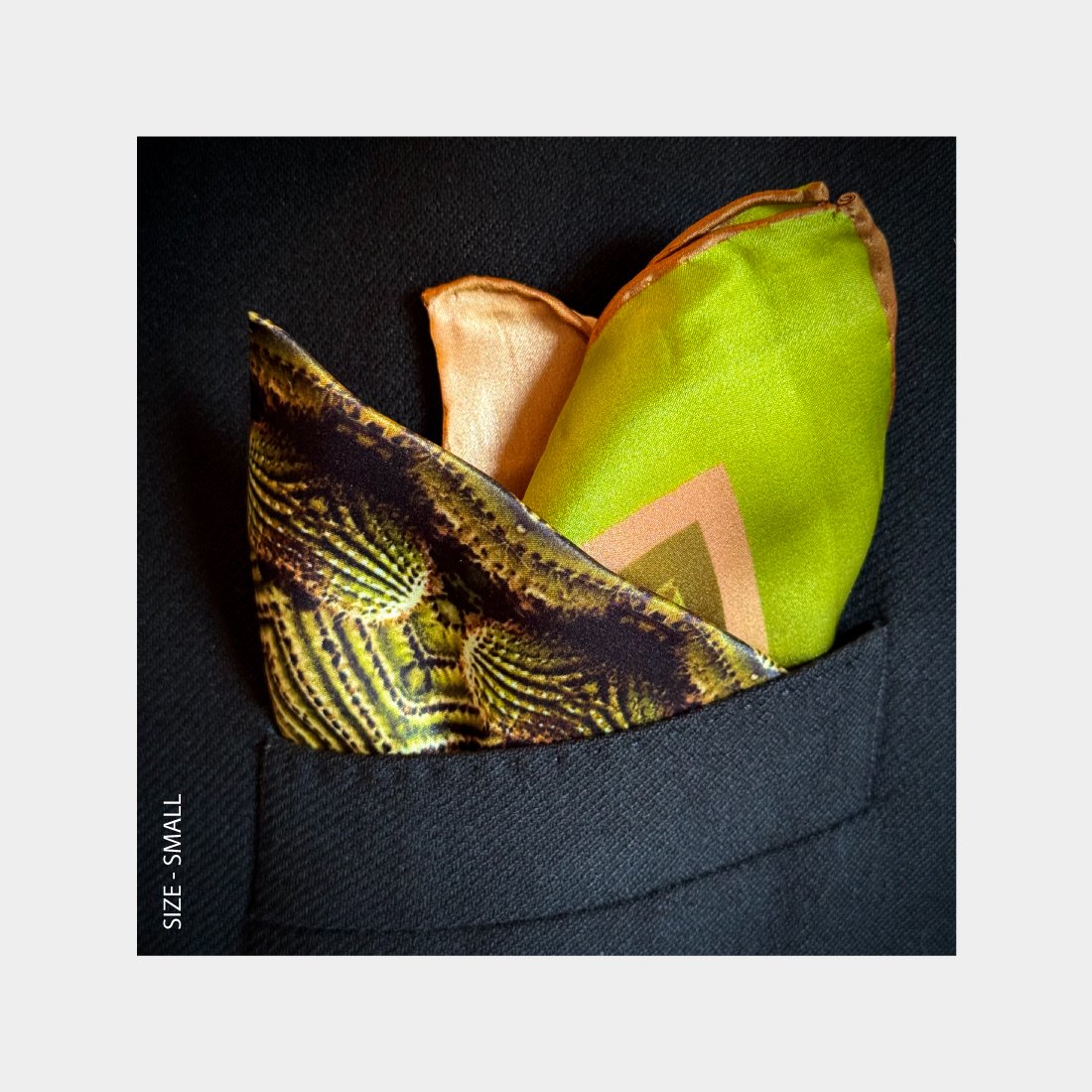 "Their Roots Grow Deep" is shown as a silk Pocket Square bursting with brillant green and earthy tones from the breast pocket of a black wool jacket.