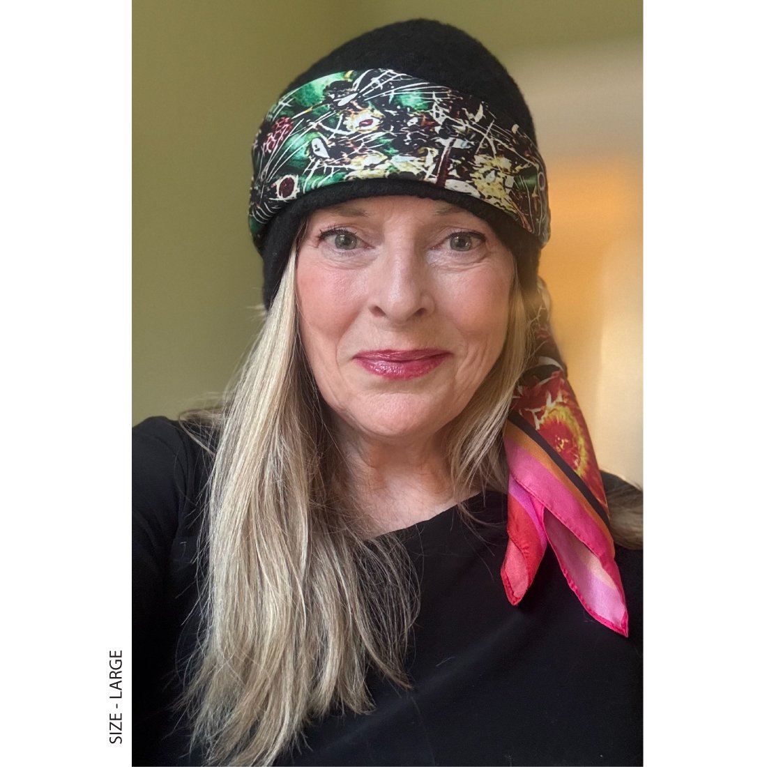 A woman with long blond hair wears "phoenix" silk scarf size large around her black felt hat. The pink borders show on her shoulder.