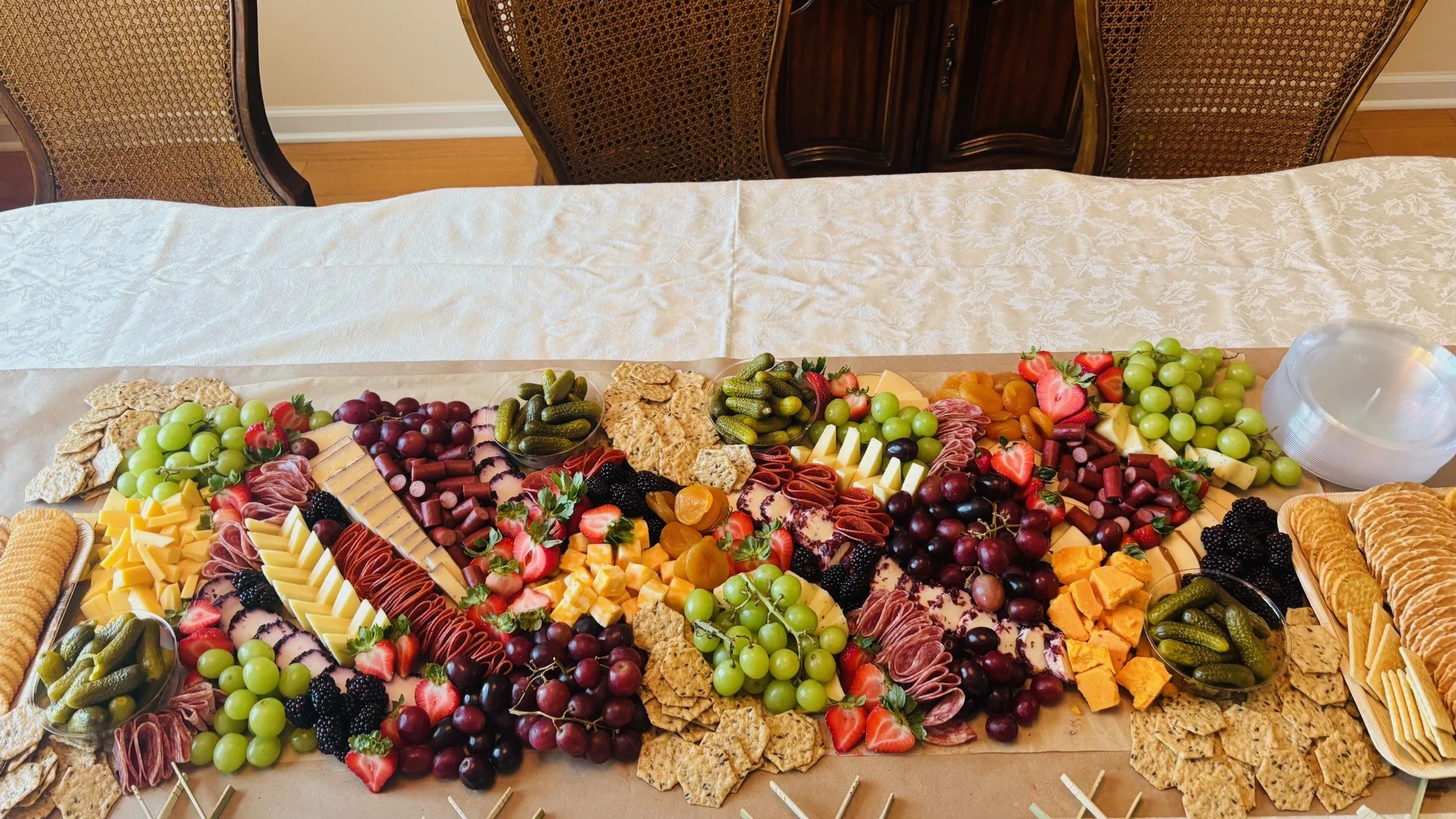 A large fruit and cheese platter with grapes, strawberries, blackberries, and various cheeses, meats, and crackers on a table spread with white tablecloth.