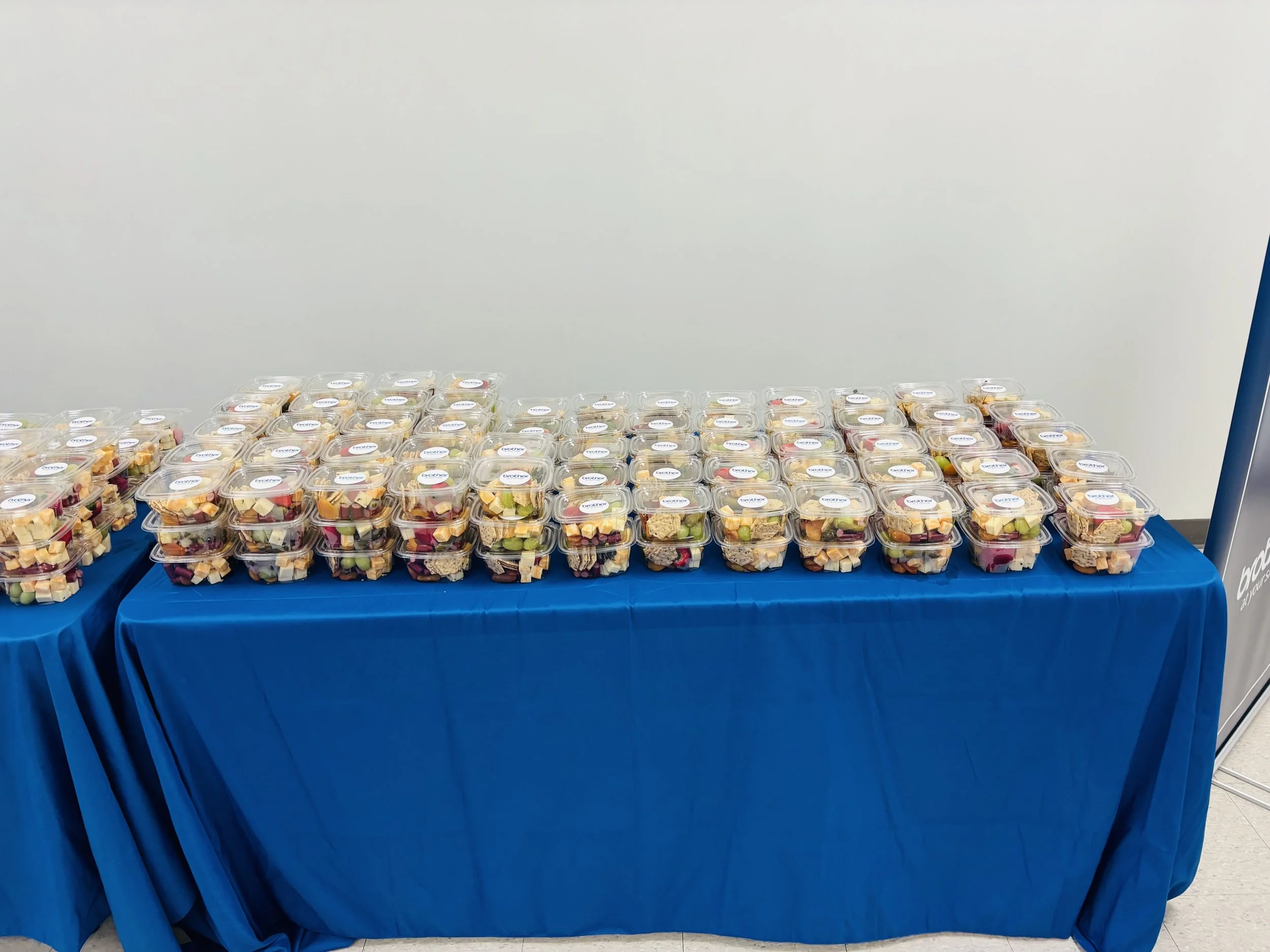 Table covered with a blue cloth, displaying multiple containers of pre-packaged fruit salad.