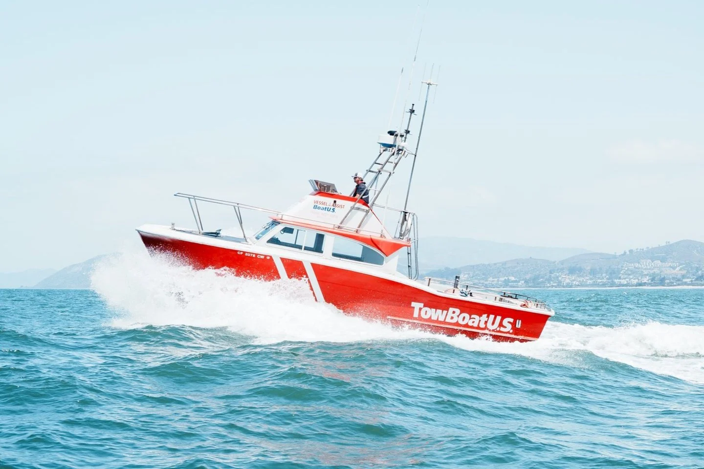 Red and white tow boat speeding through water with mountains in the background