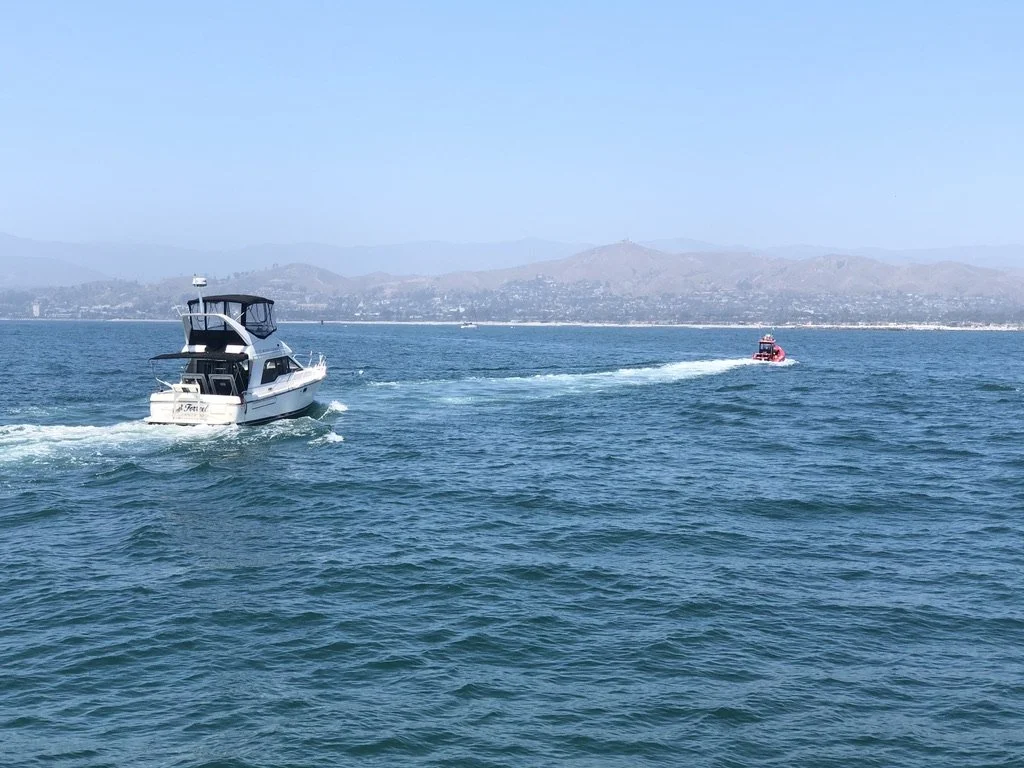 A white yacht sailing on the water with a smaller red boat trailing behind on a hazy day, with hills in the background.