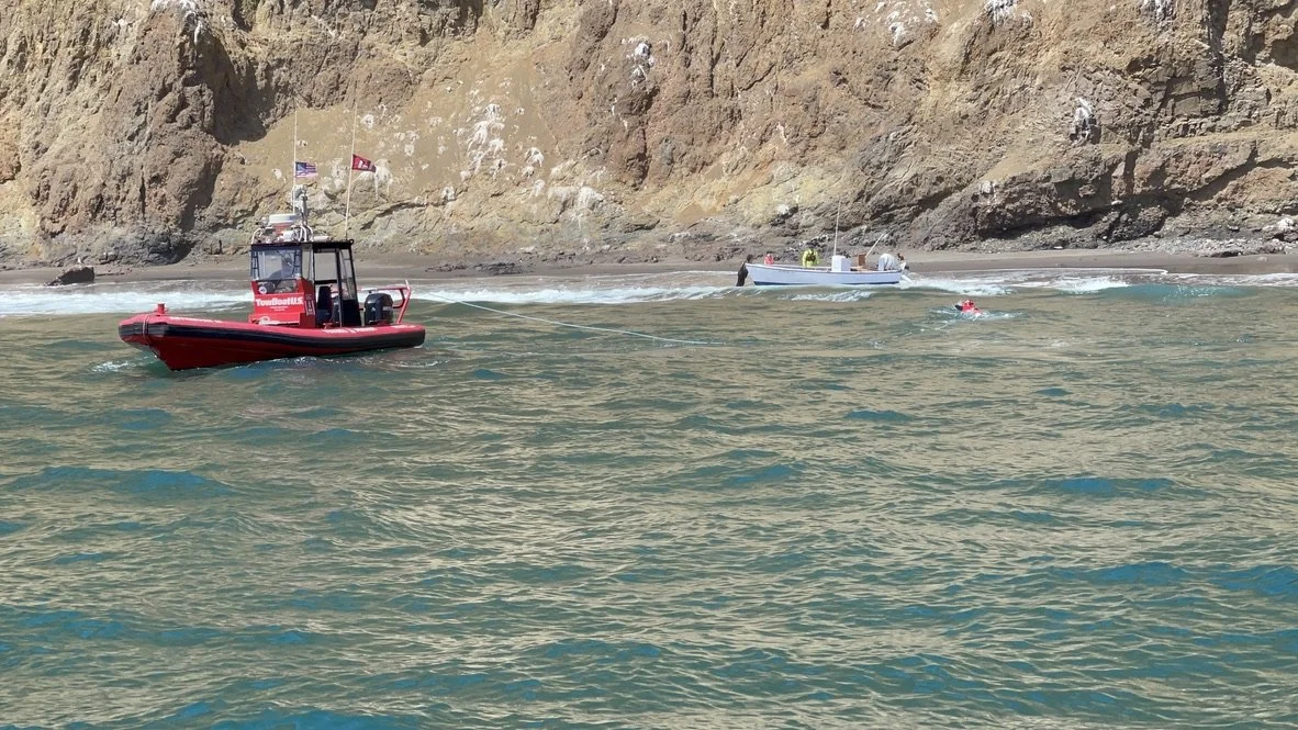 A red rescue boat and a smaller white boat in the water near a rocky shoreline, with a person swimming nearby.