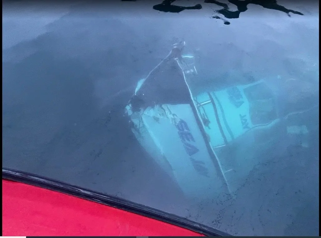 A boat is submerged upside down in a body of water, with a visible push/pull sign on its side.