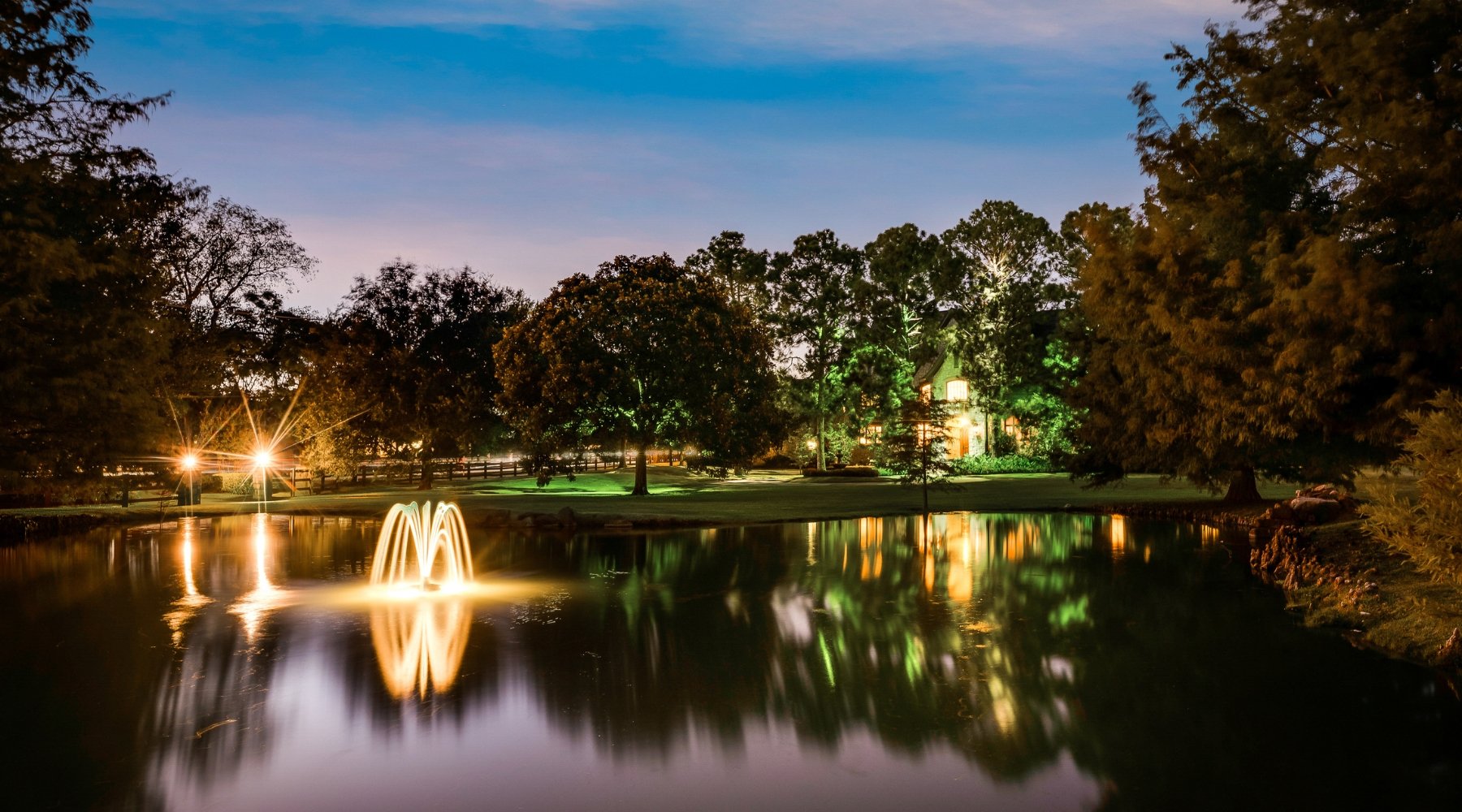 Twilight view of a luxury estate home sold by Lily Moore in Colleyville, Texas, with a pond, fountain and mature trees