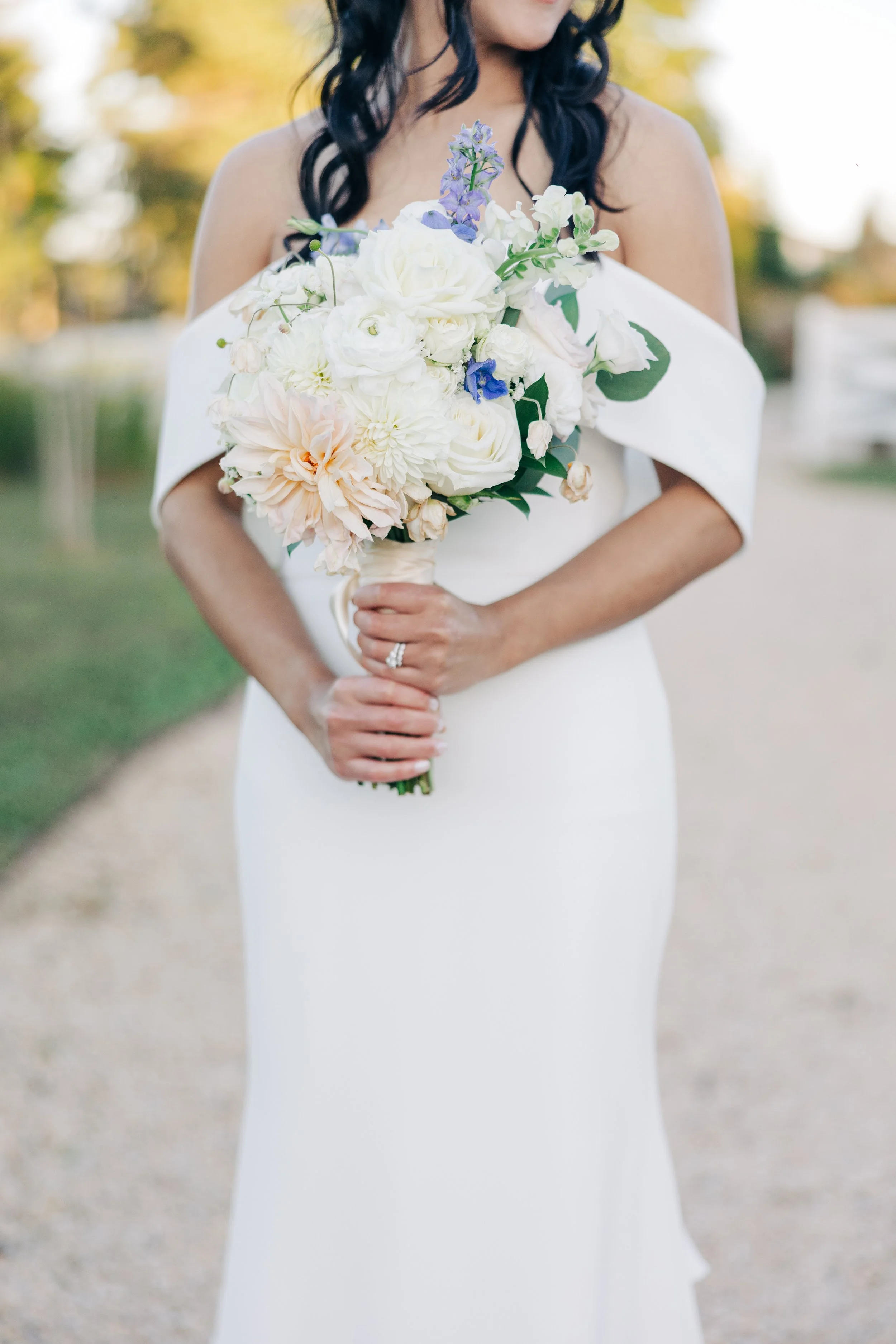 A woman dressed in a white wedding gown holding a bouquet of white, peach, and purple flowers.