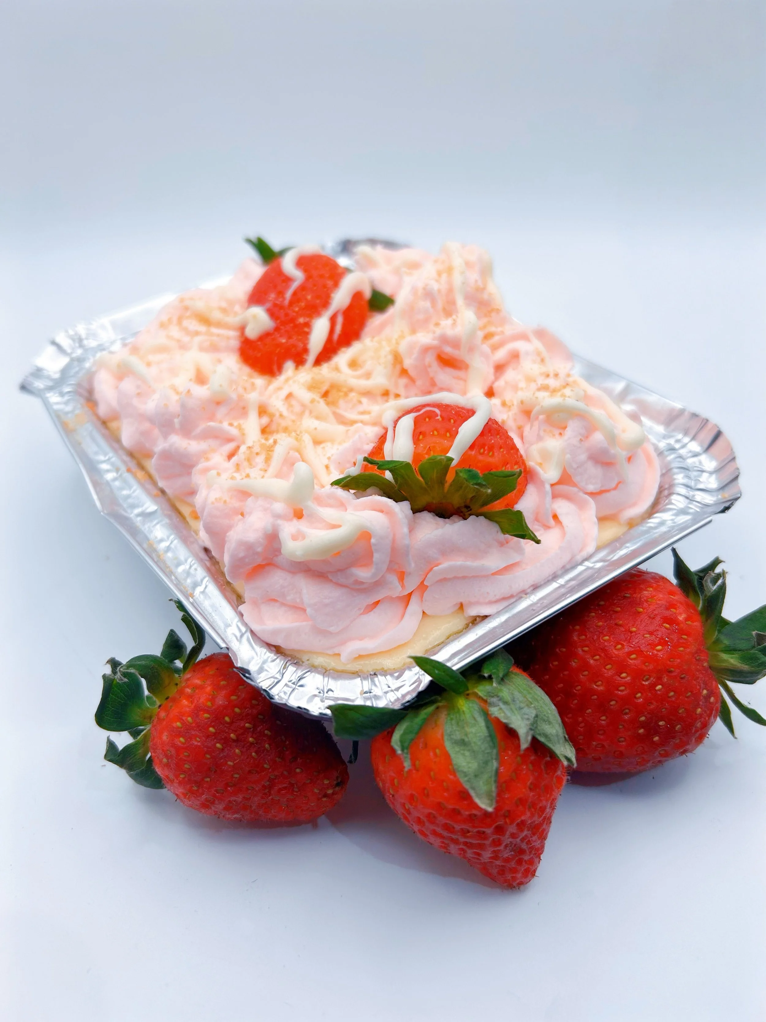 Strawberry and pocky cookie cheesecake dessert with strawberries and whipped cream in a silver container, placed on a white surface.