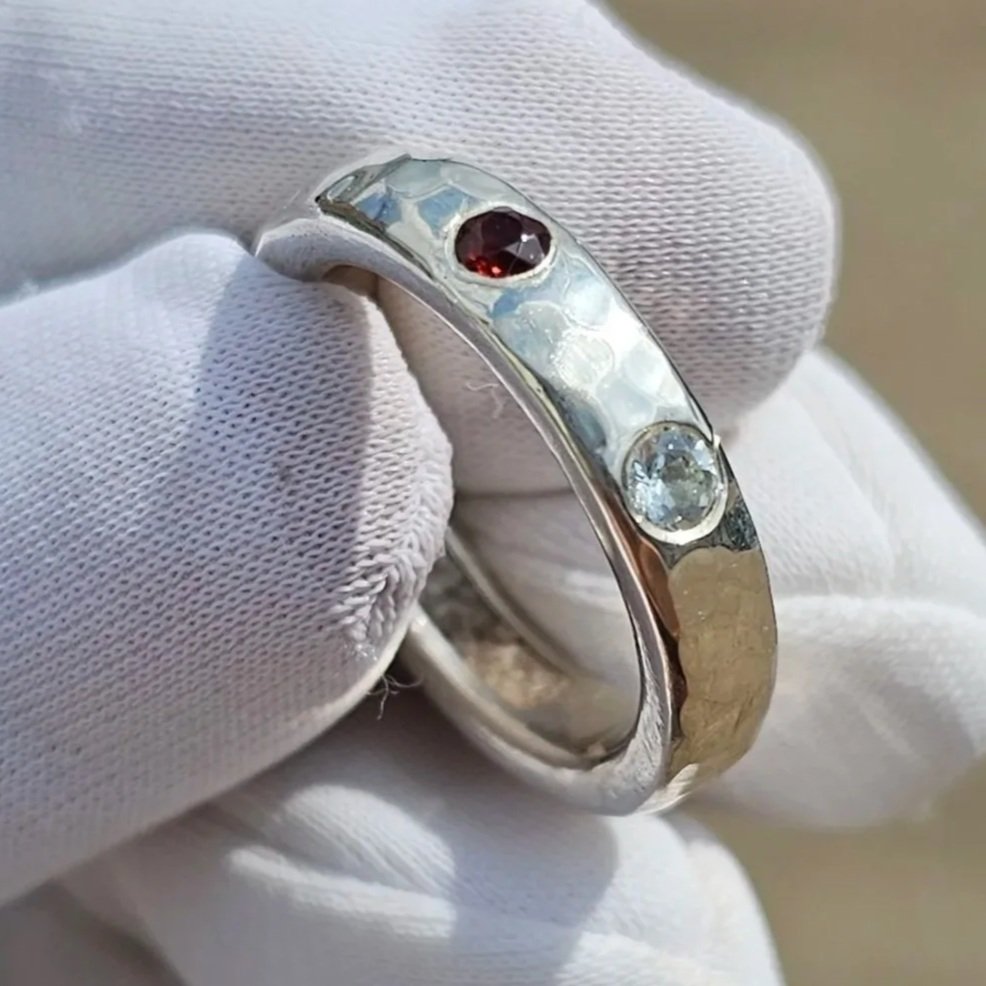 Close-up photo of a silver ring with three gemstones, held by a person's hand wearing a white glove.