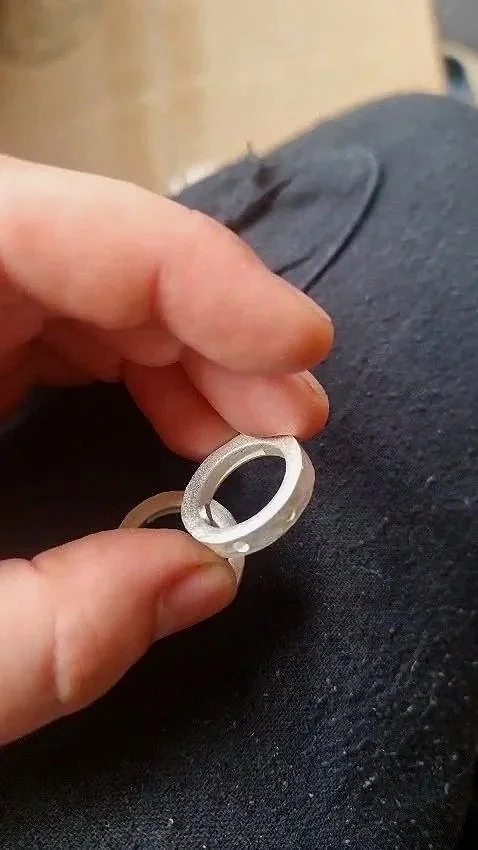 Person holding silver ring or washer close-up with dark fabric background.
