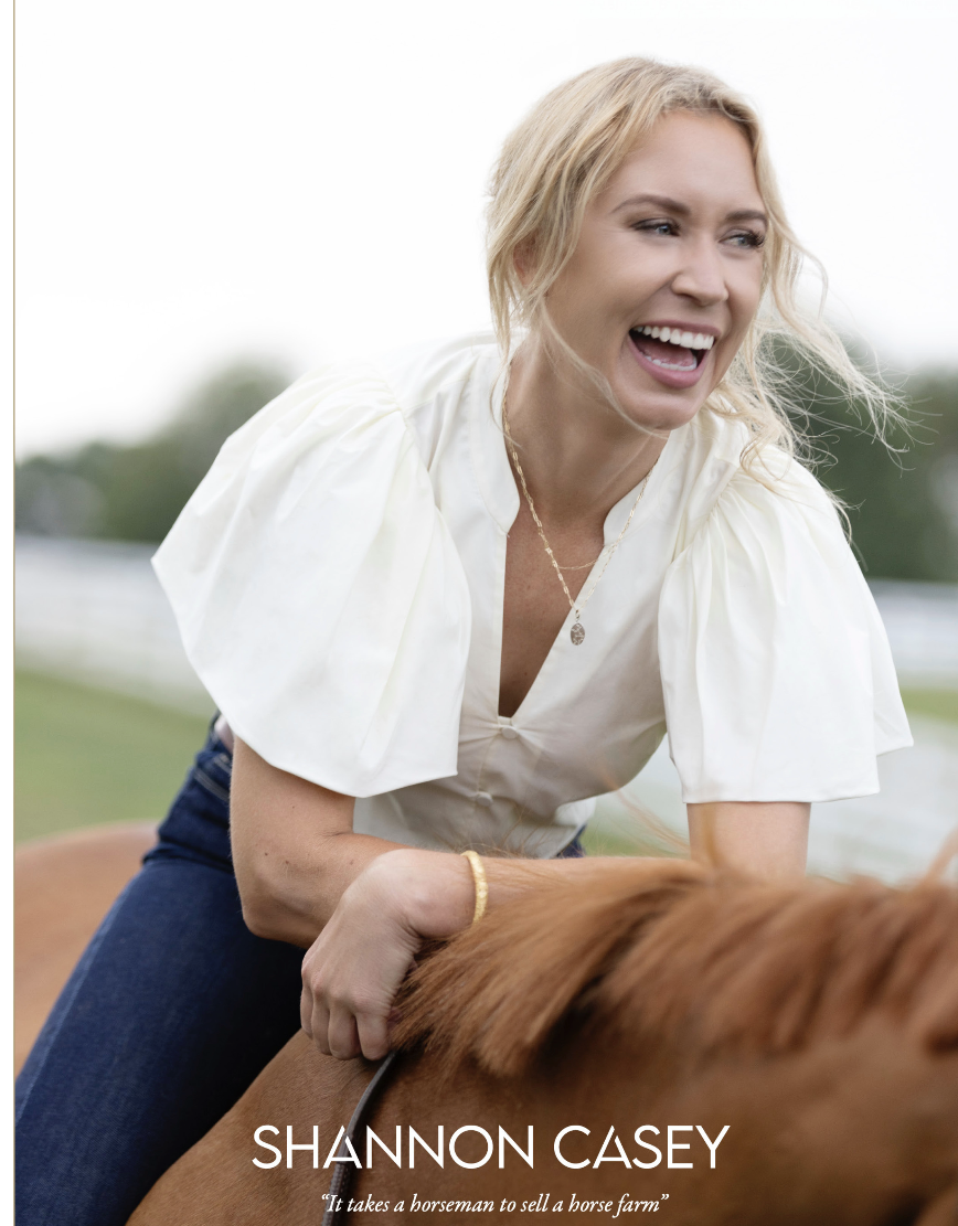 Woman smiling next to a brown horse with a background of trees and sunlight.