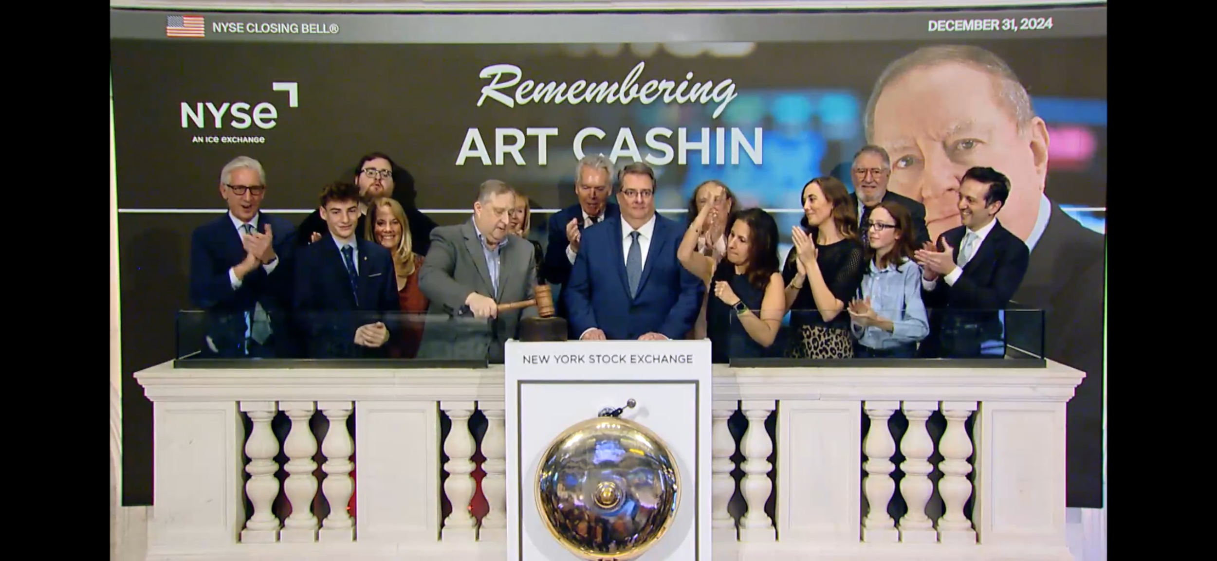 Group of people on a stage at the New York Stock Exchange celebrating Art Cashin with a large banner behind them that reads 'Remembering Art Cashin' and the date December 31, 2024.