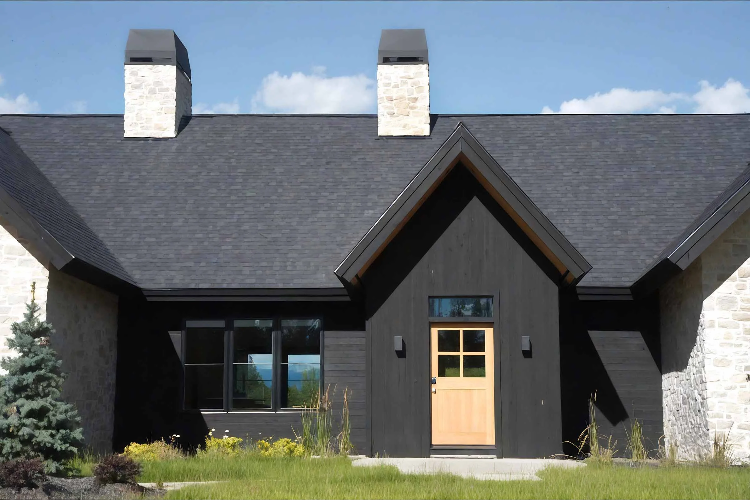 Modern black exterior and wood entry door of a custom mountain home with gabled roofs and chimneys, engineered for Idaho’s climate and seasonal demands.