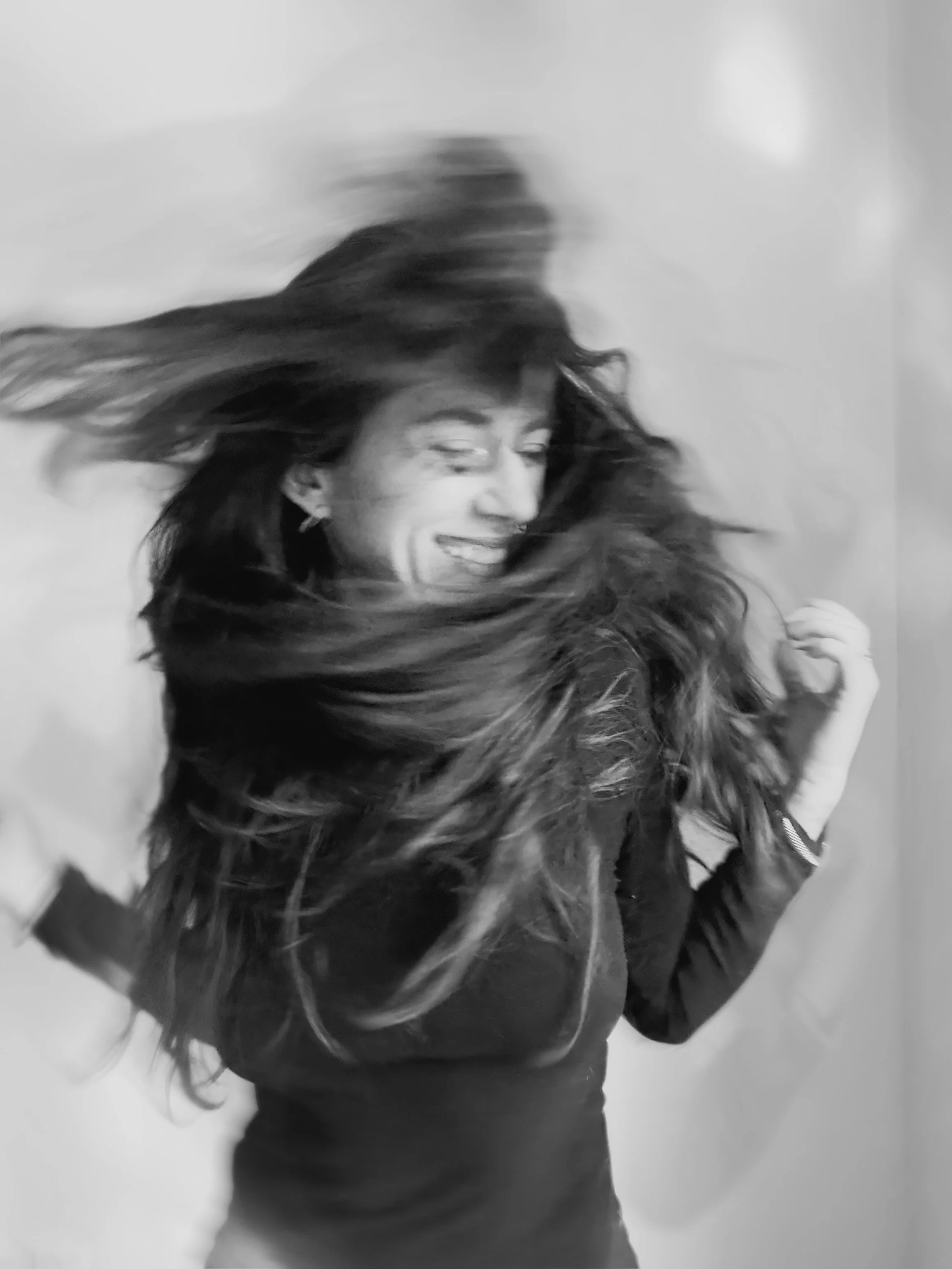 Black and white photo of a woman with long hair spinning and smiling, with her hair in motion around her face.