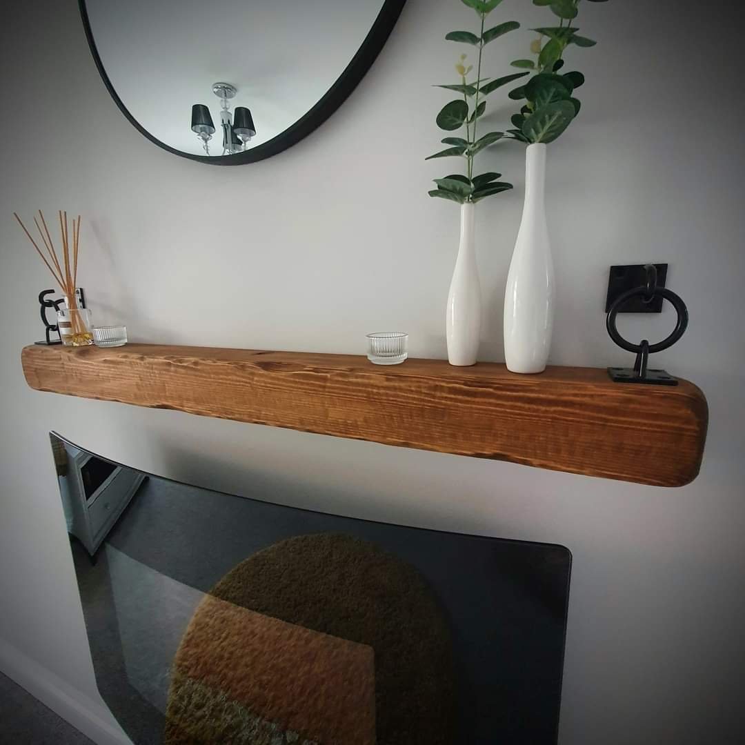Wooden mantel shelf with decorative items, including white vases, a round mirror above, and a curved glass fireplace below.