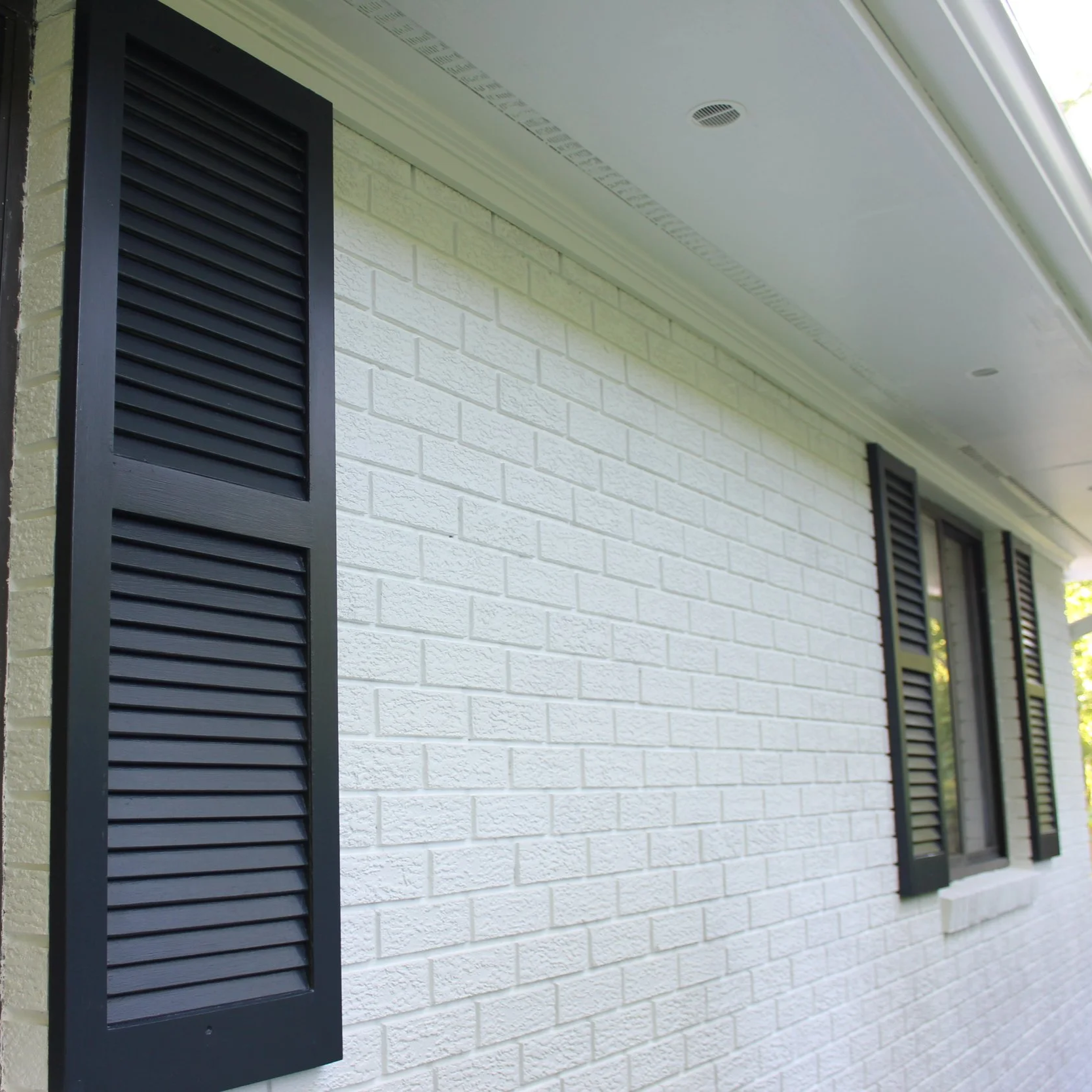 Exterior of a house showing three black window shutters on a white brick wall.