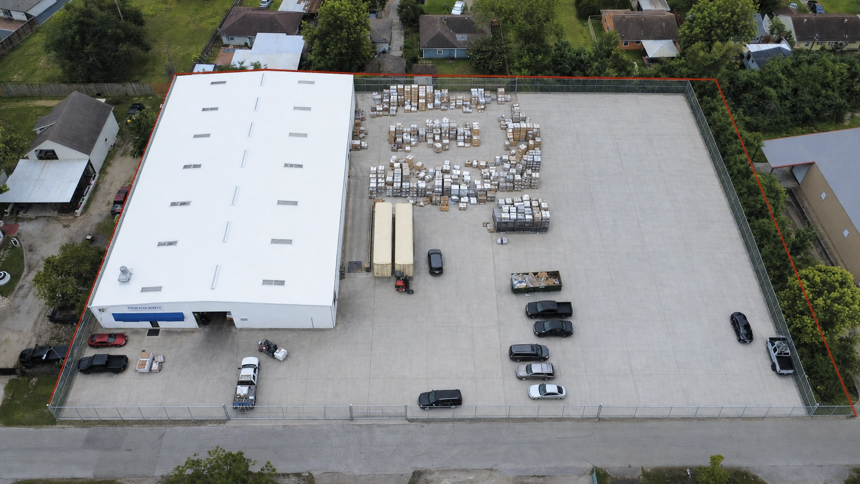 Aerial view of a commercial property with two large white buildings, a parking lot with multiple recreational vehicles, and a row of elongated blue structures labeled "RV & BOAT STORAGE". Surrounding greenery and a rural area are also visible.