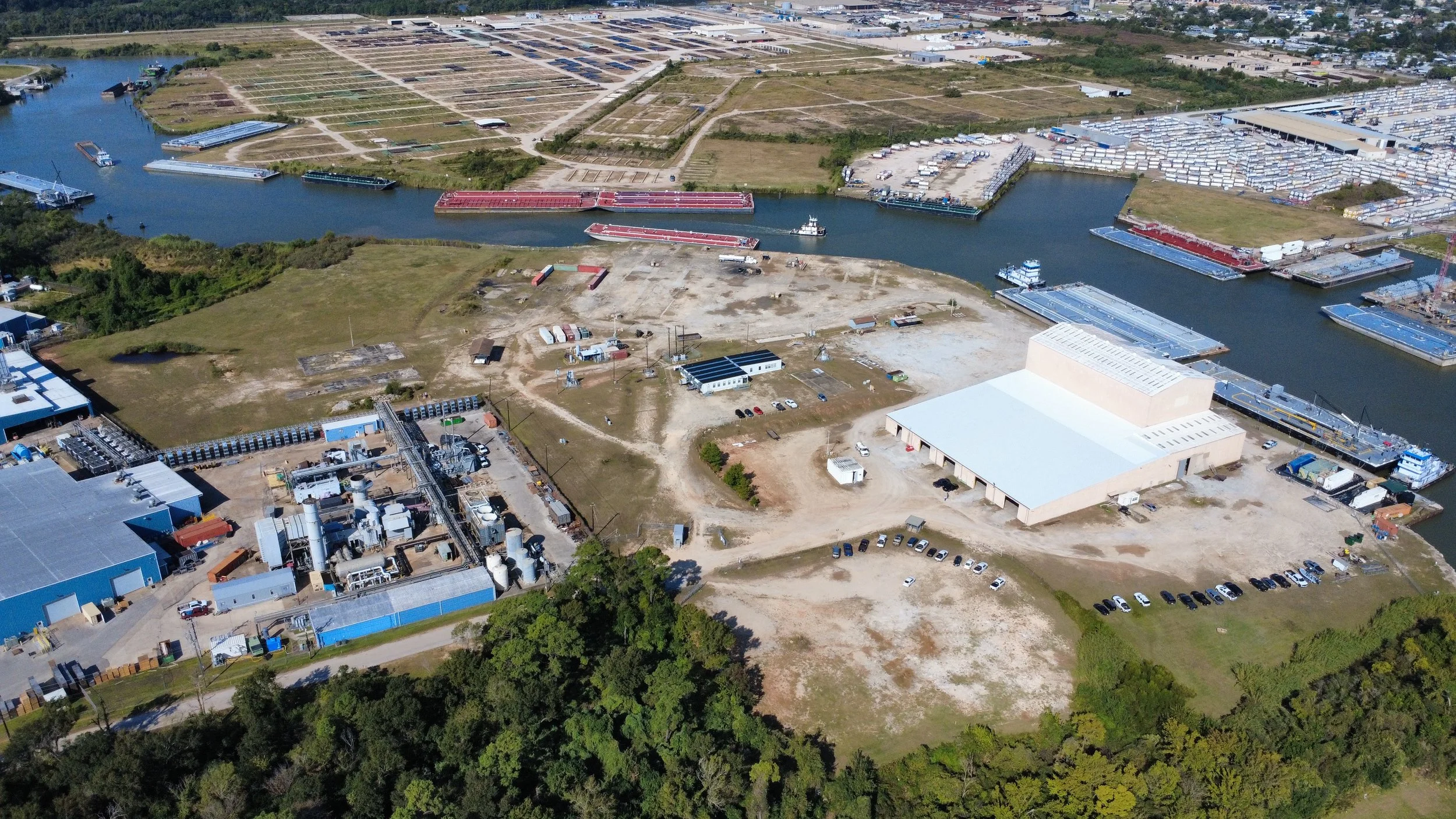 Aerial view of a commercial or industrial area with large warehouse buildings, surrounded by residential neighborhoods and green trees.