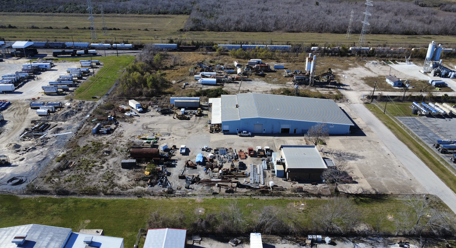 Aerial view of a commercial building with a brown roof, surrounded by parking lots with several cars, and neighboring industrial and commercial buildings in a cityscape.
