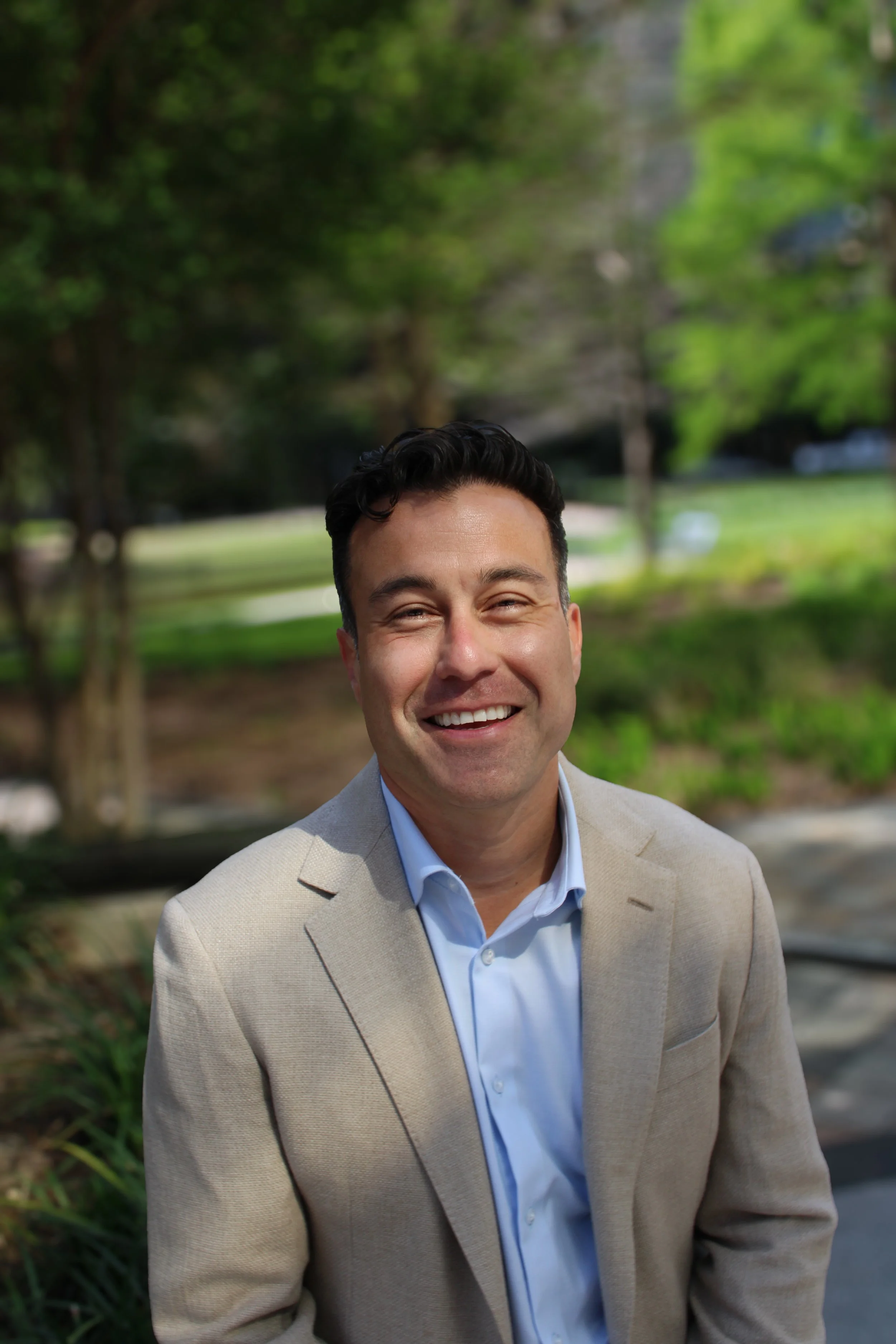 A man in a light blue blazer and white shirt leaning against a brick wall outside a building.