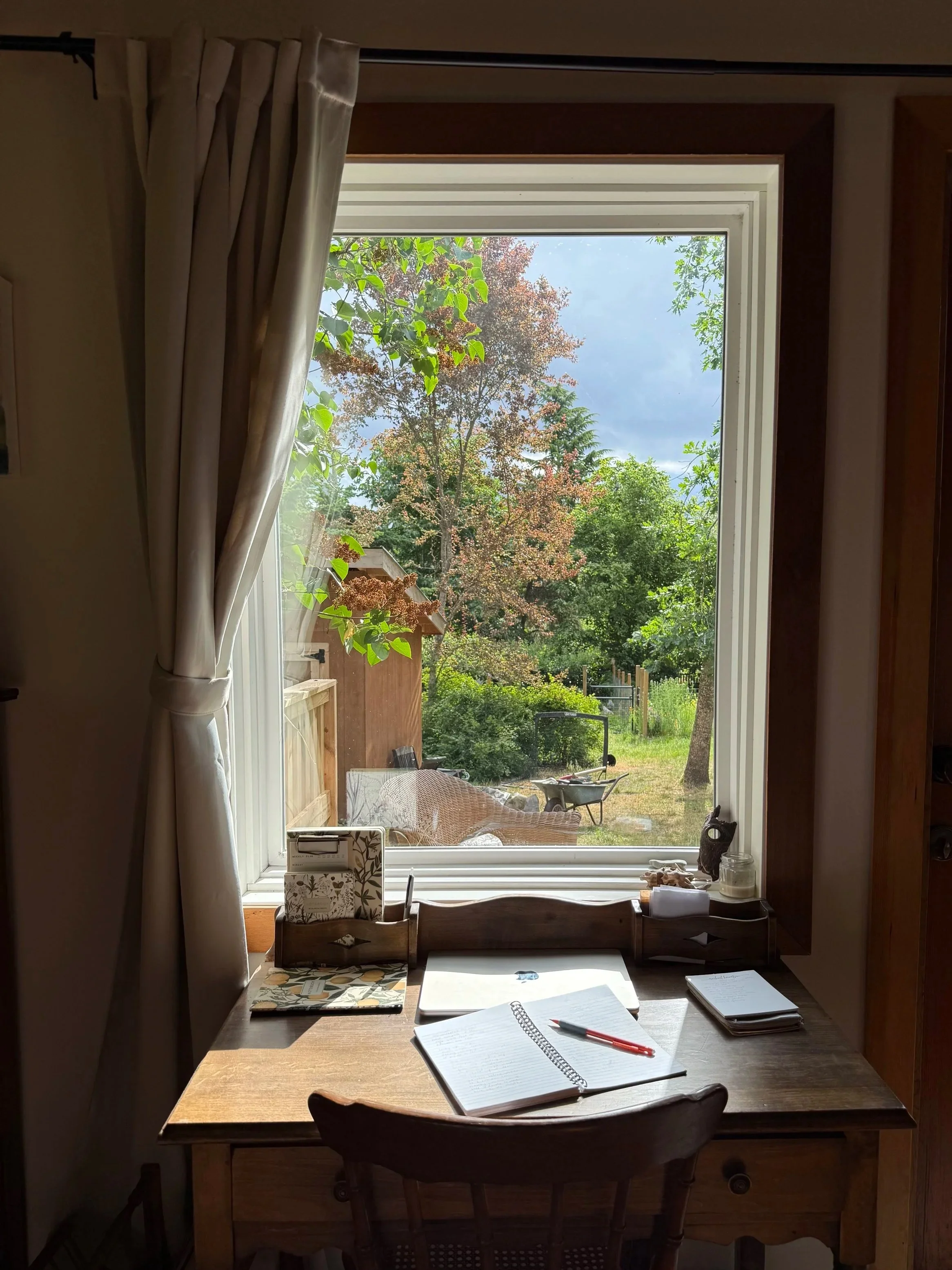 Desk with open journal for writing poetry on it that faces a window that overlooks a garden.