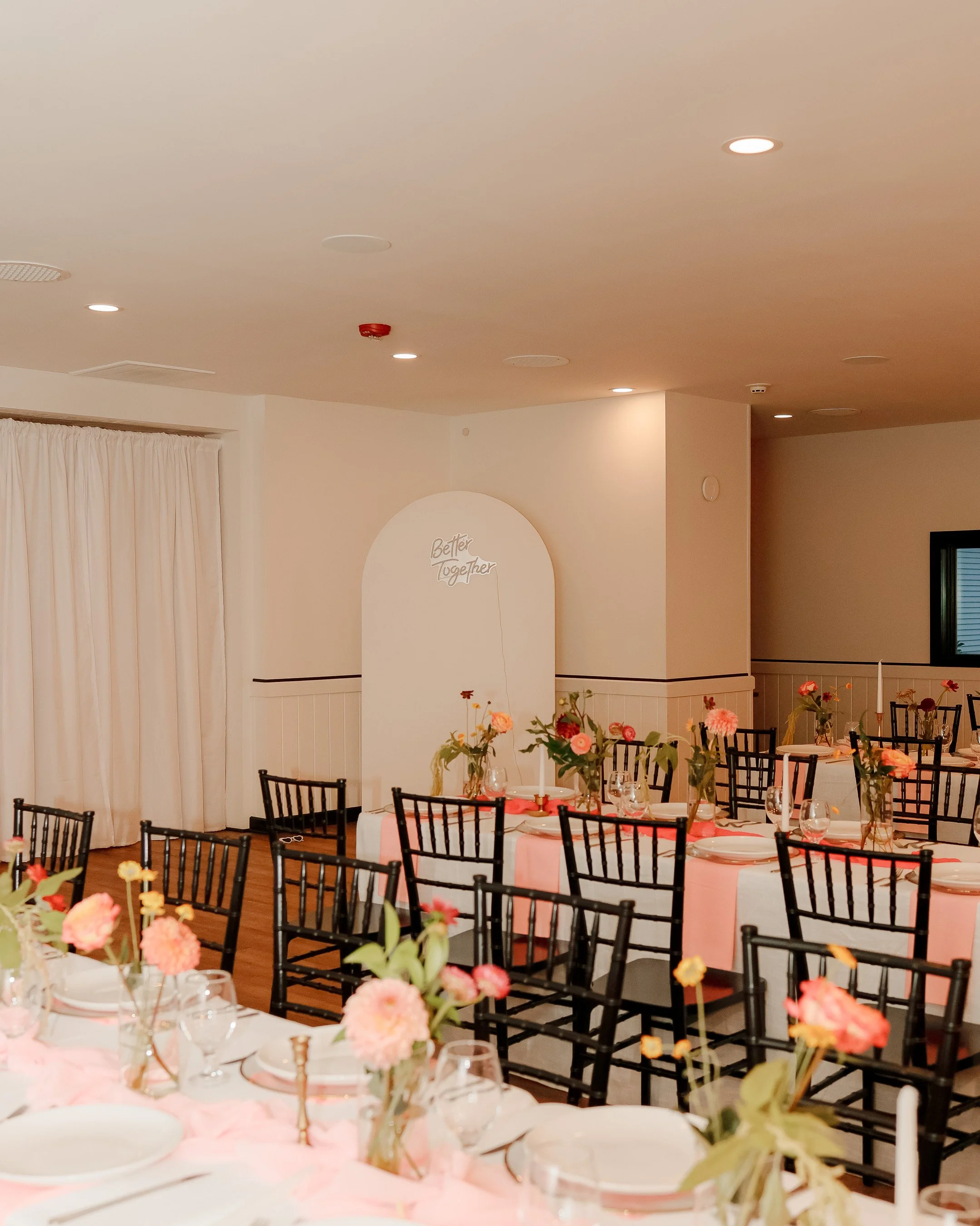 Reception tables set with white linens, glassware, and floral centerpieces inside the event hall at Fairhaven Inn & Events.